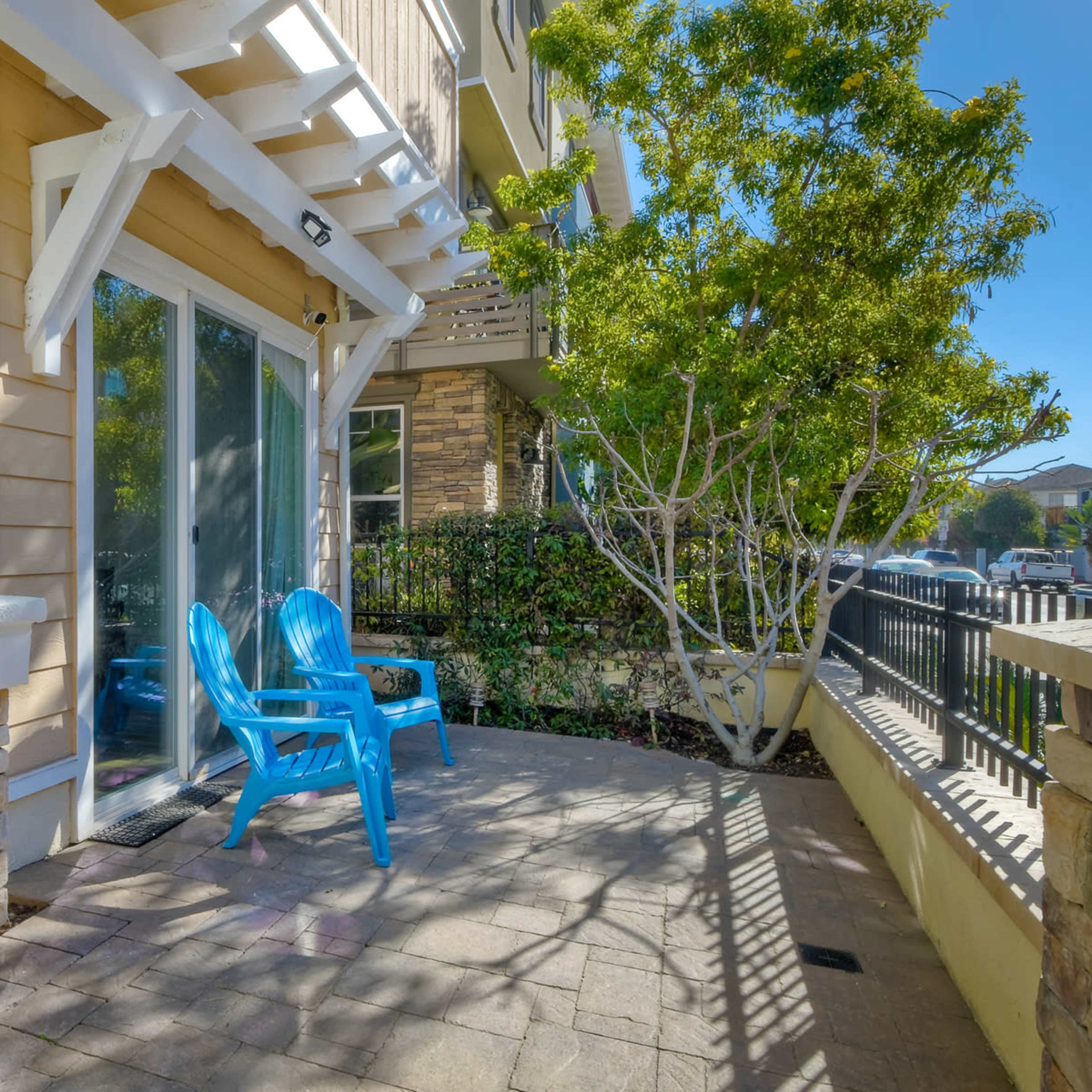 A patio area with two blue chairs, surrounded by greenery and a stone wall.