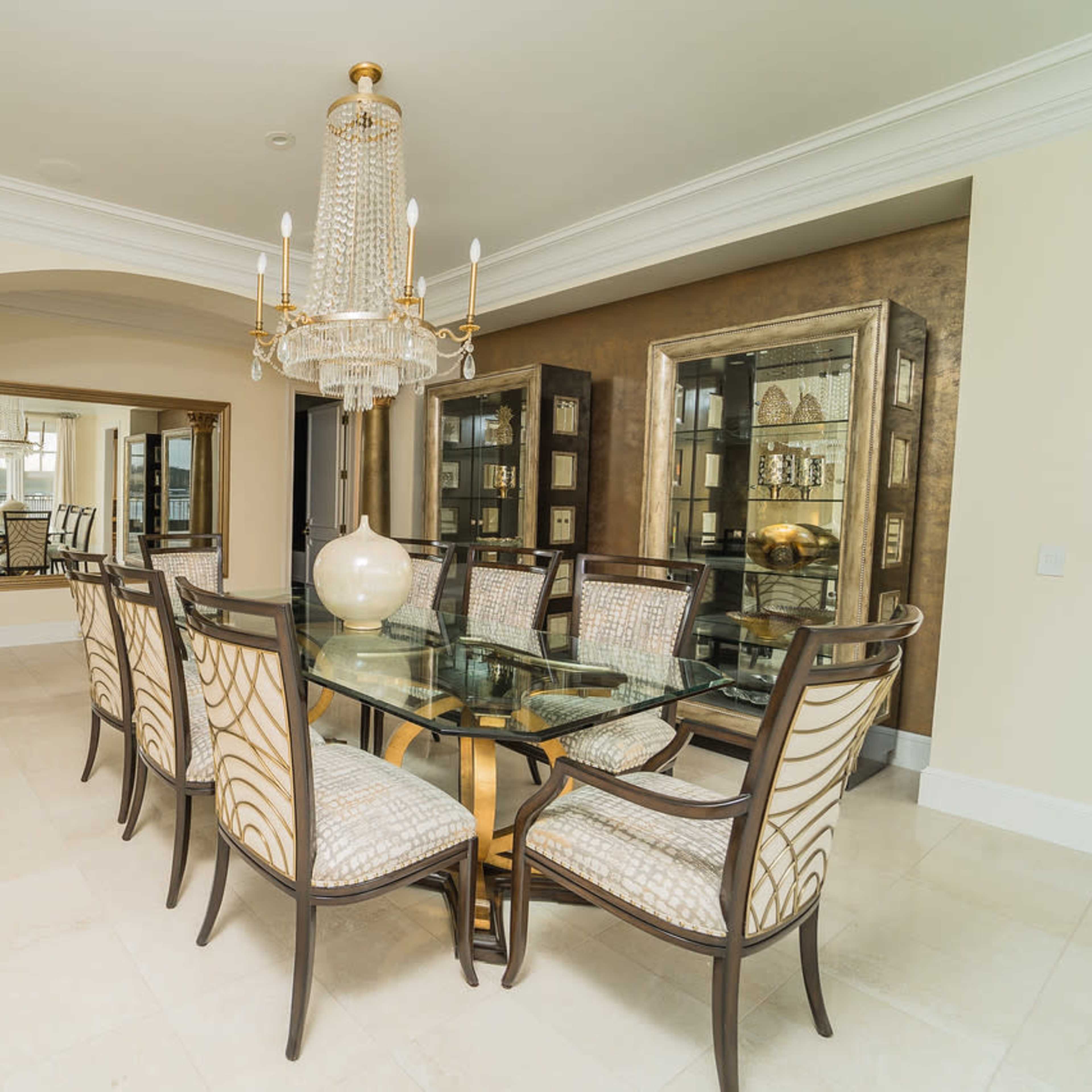 A spacious dining room featuring a glass dining table surrounded by upholstered chairs, a large chandelier, and decorative mirrors on the walls.