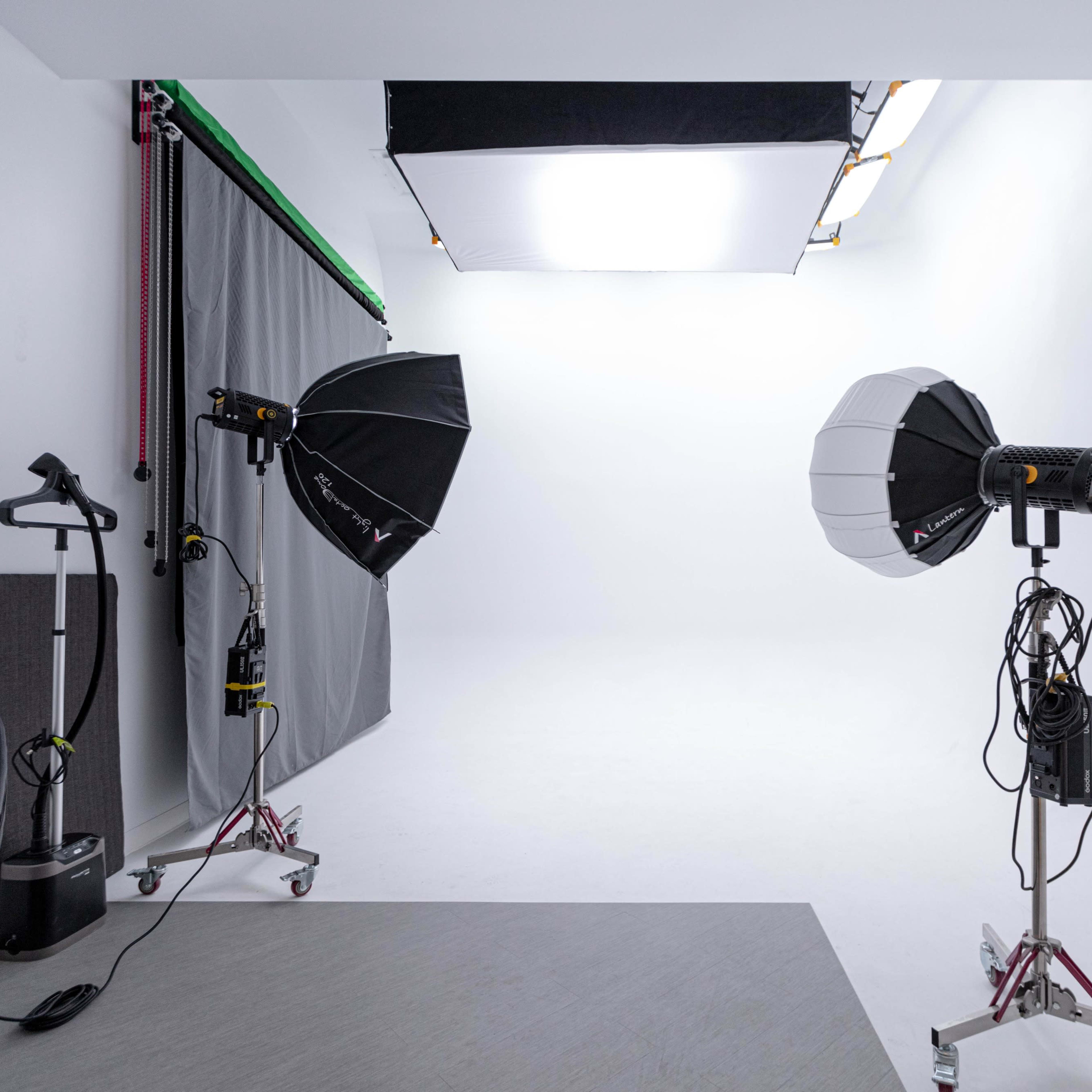 A photography studio with two lighting setups, a gray backdrop, and a black seating area.