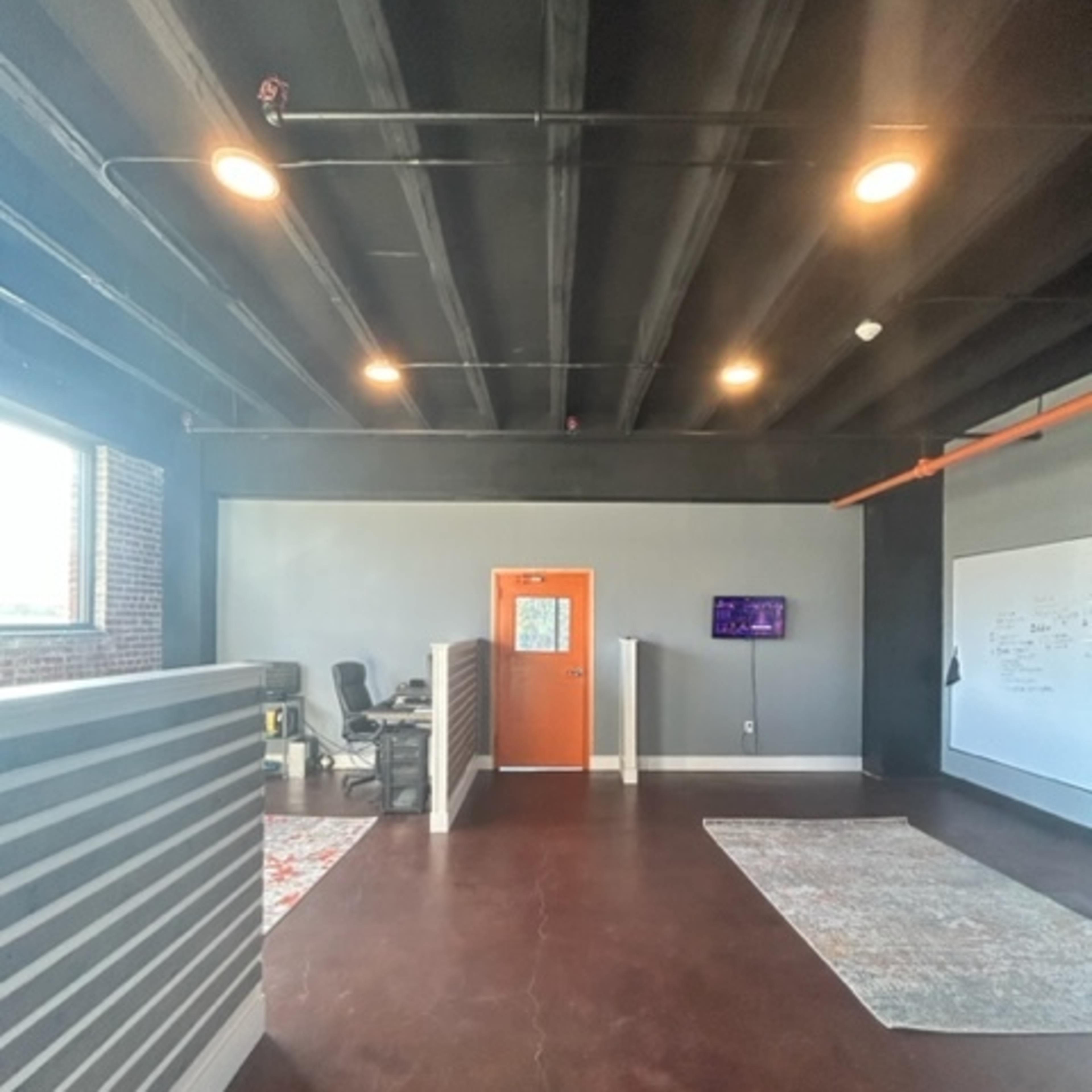 An open office space with orange accents, two rugs on a dark floor, and a chair visible behind a partition.