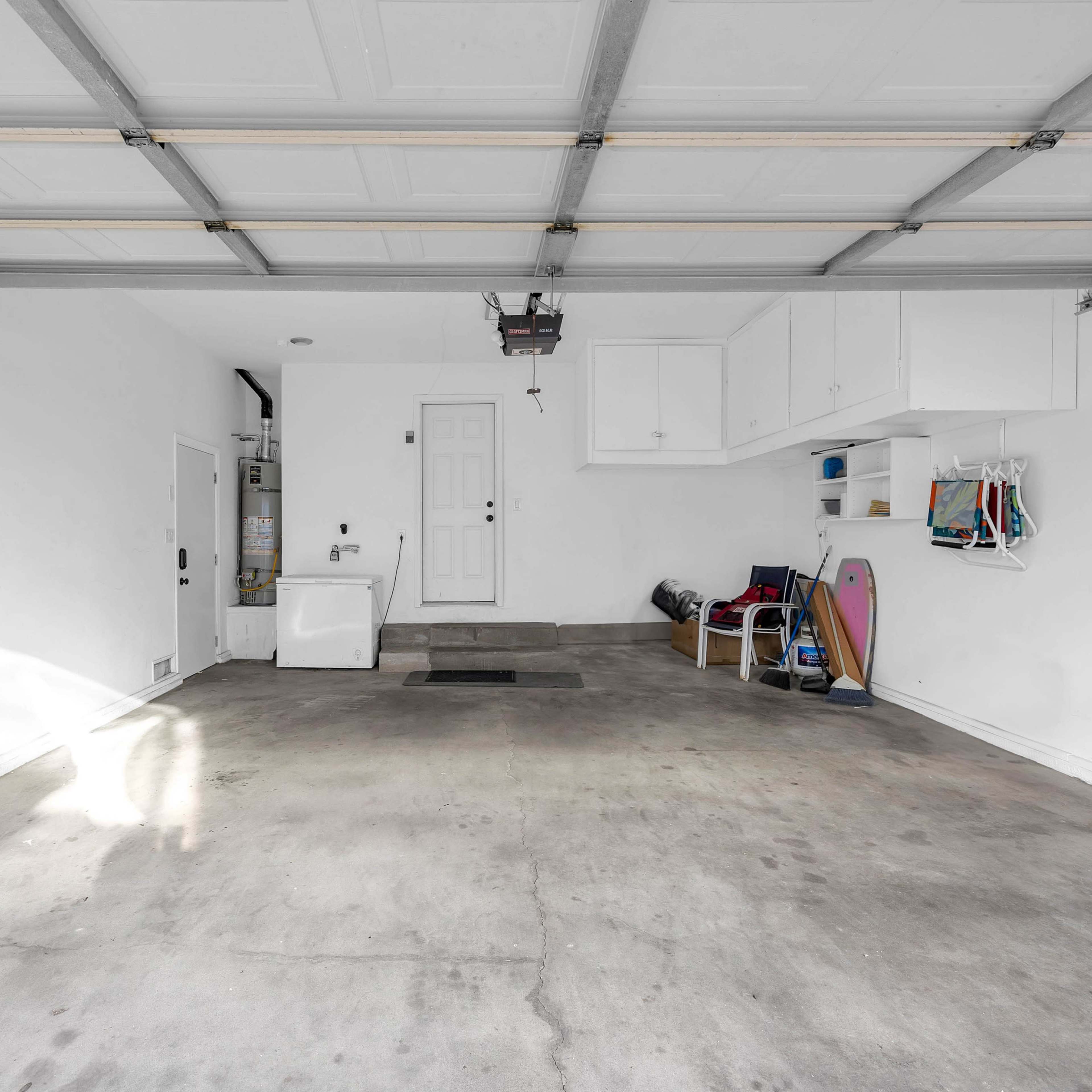 An empty garage with a concrete floor, a white door, and storage items neatly placed along the walls.