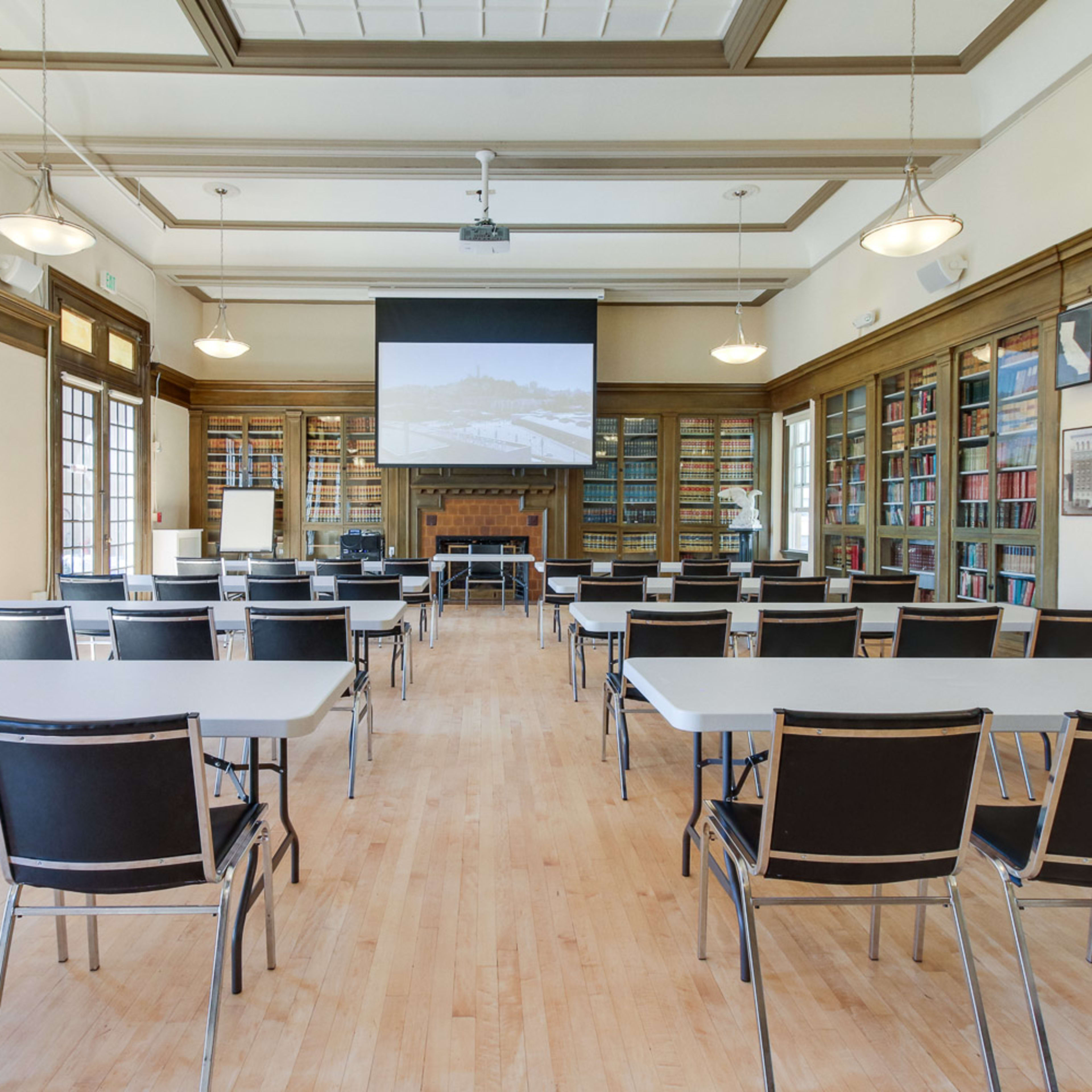 A conference room with rows of chairs and tables facing a projection screen, flanked by bookshelves.