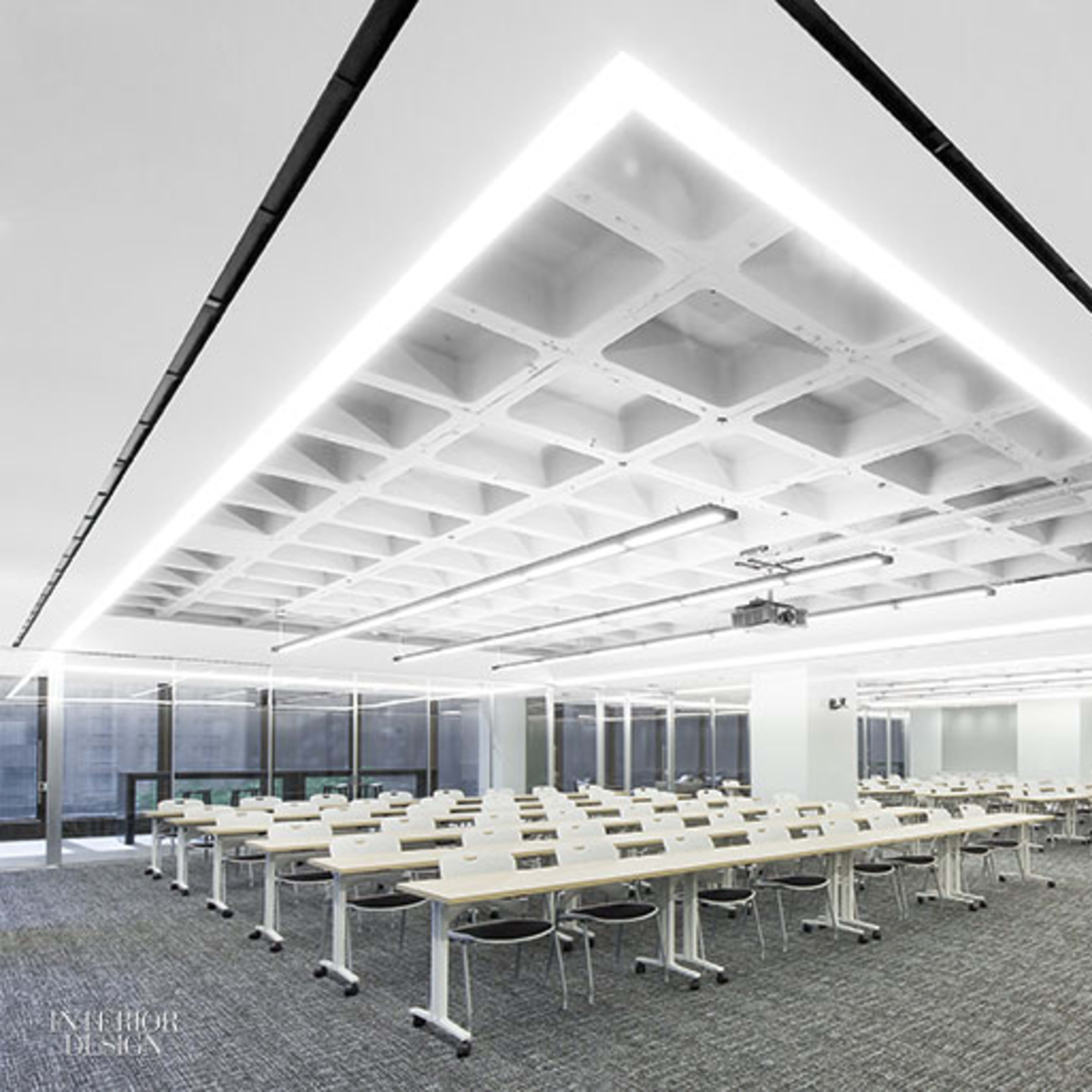A modern conference room features rows of white tables and chairs under a coffered ceiling with linear lighting.