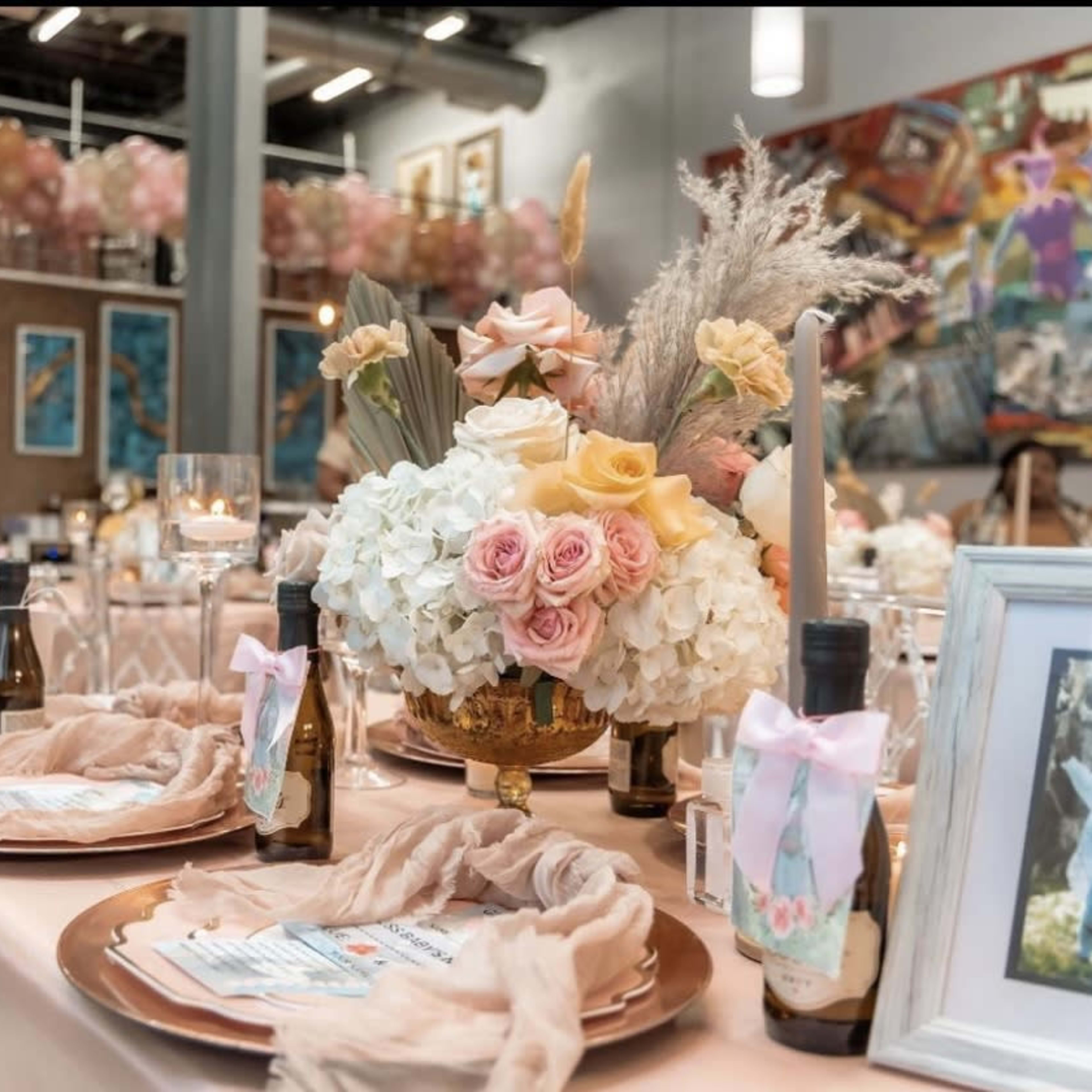 A elegantly set table for an event, featuring floral centerpieces, decorative plates, and bottles alongside a backdrop of balloon decorations.