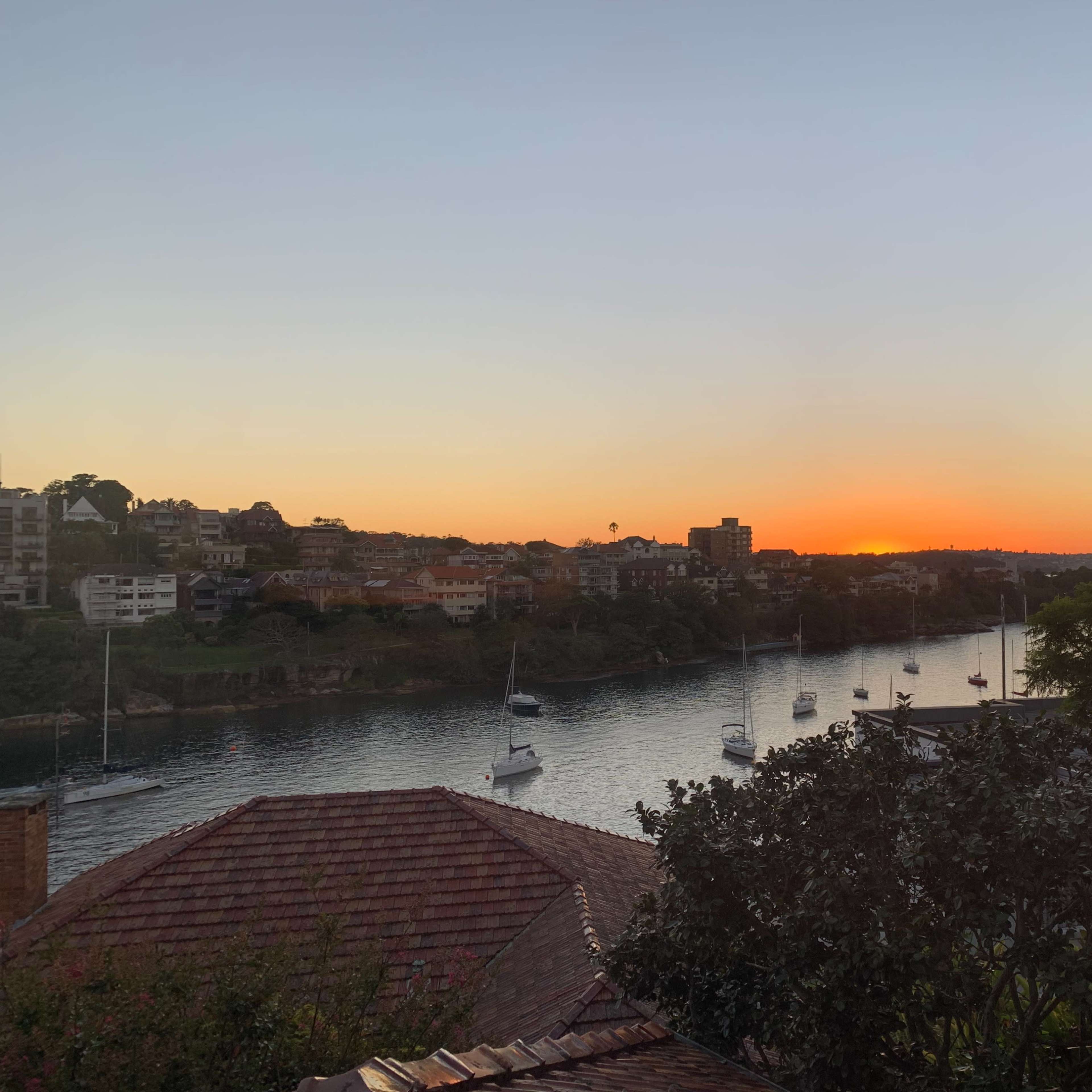 A river with sailboats is visible in the foreground as the sun sets behind the horizon.
