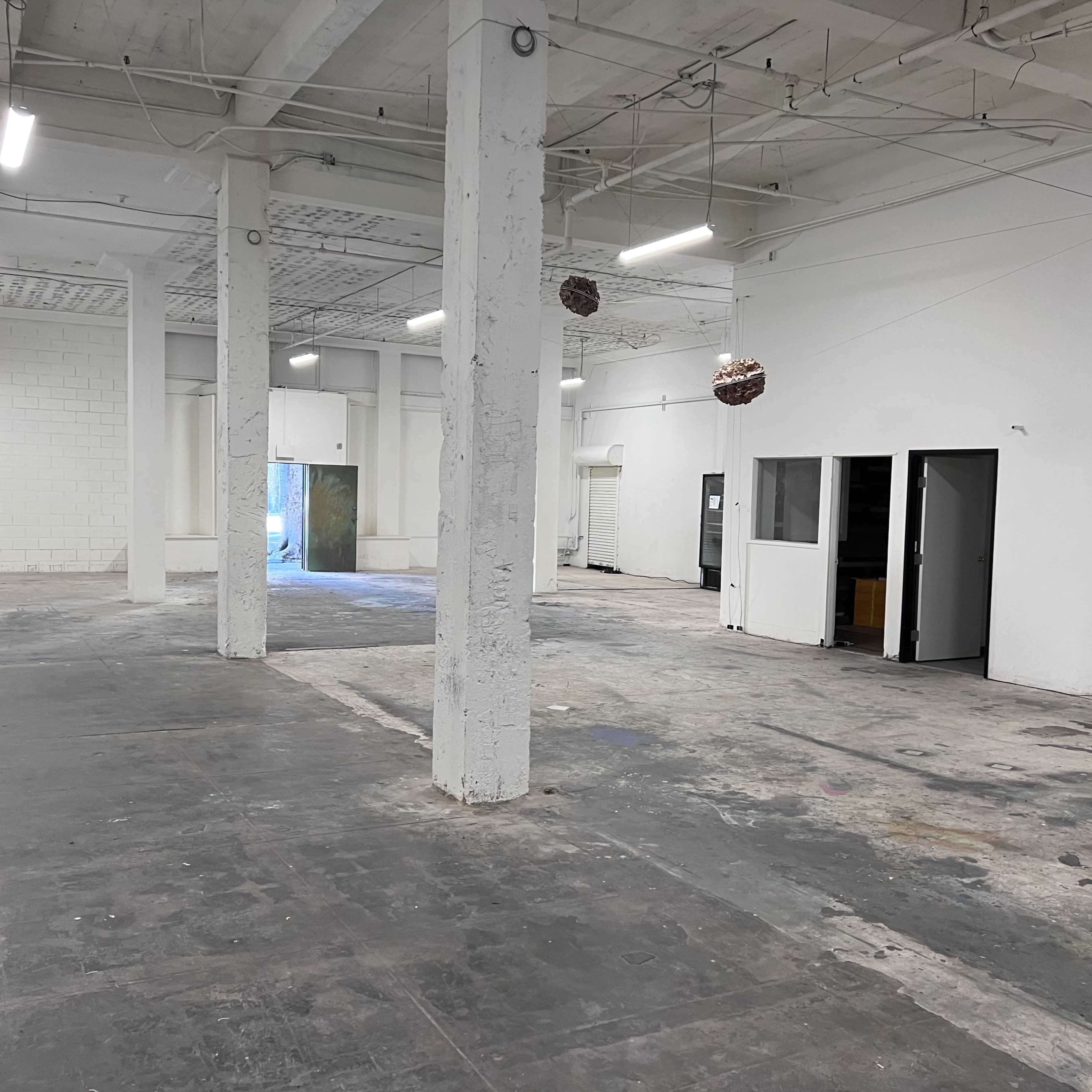 A spacious, empty interior of a building with concrete floors, white walls, and several columns.