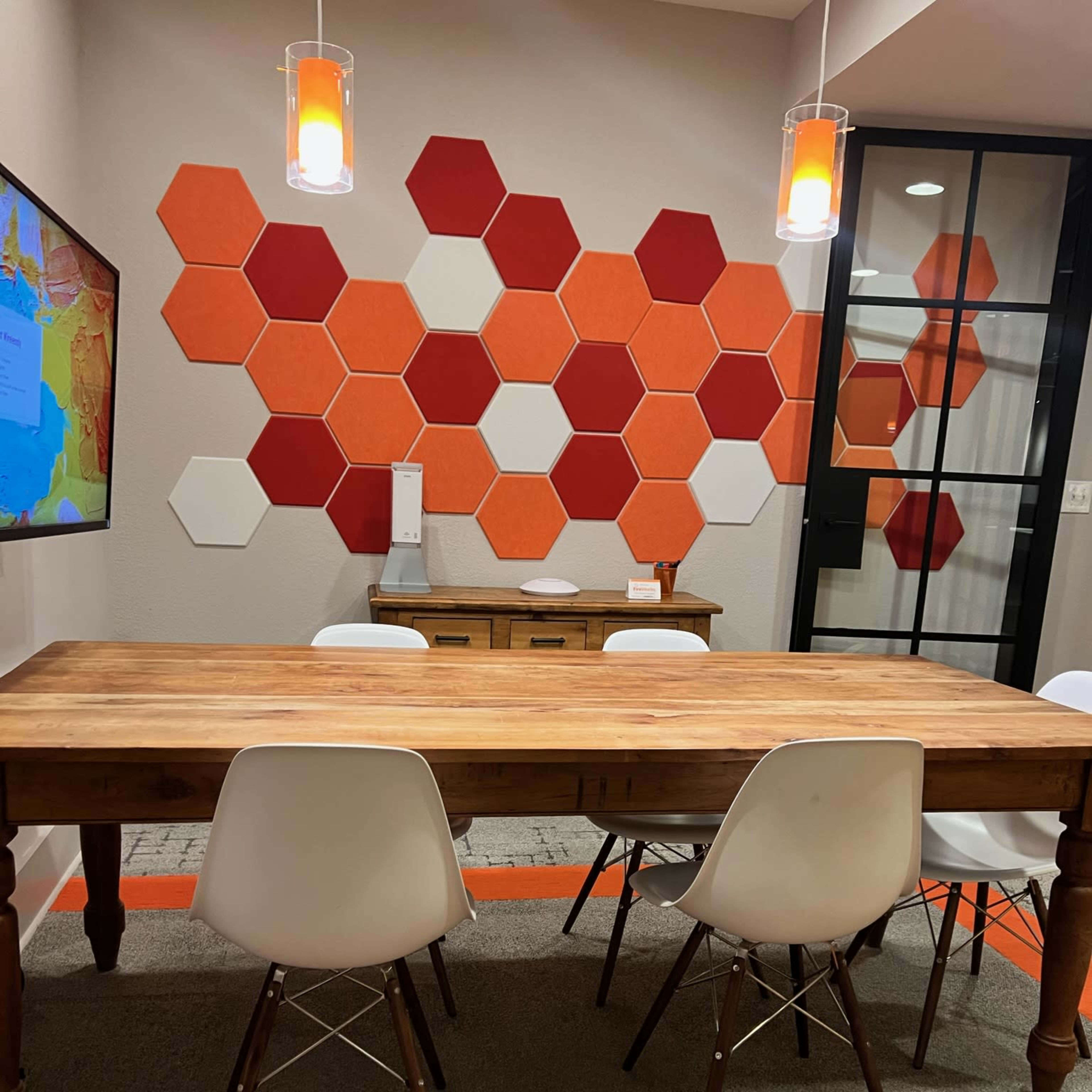 A wooden table surrounded by white chairs is set against a wall adorned with red and orange hexagonal tiles.