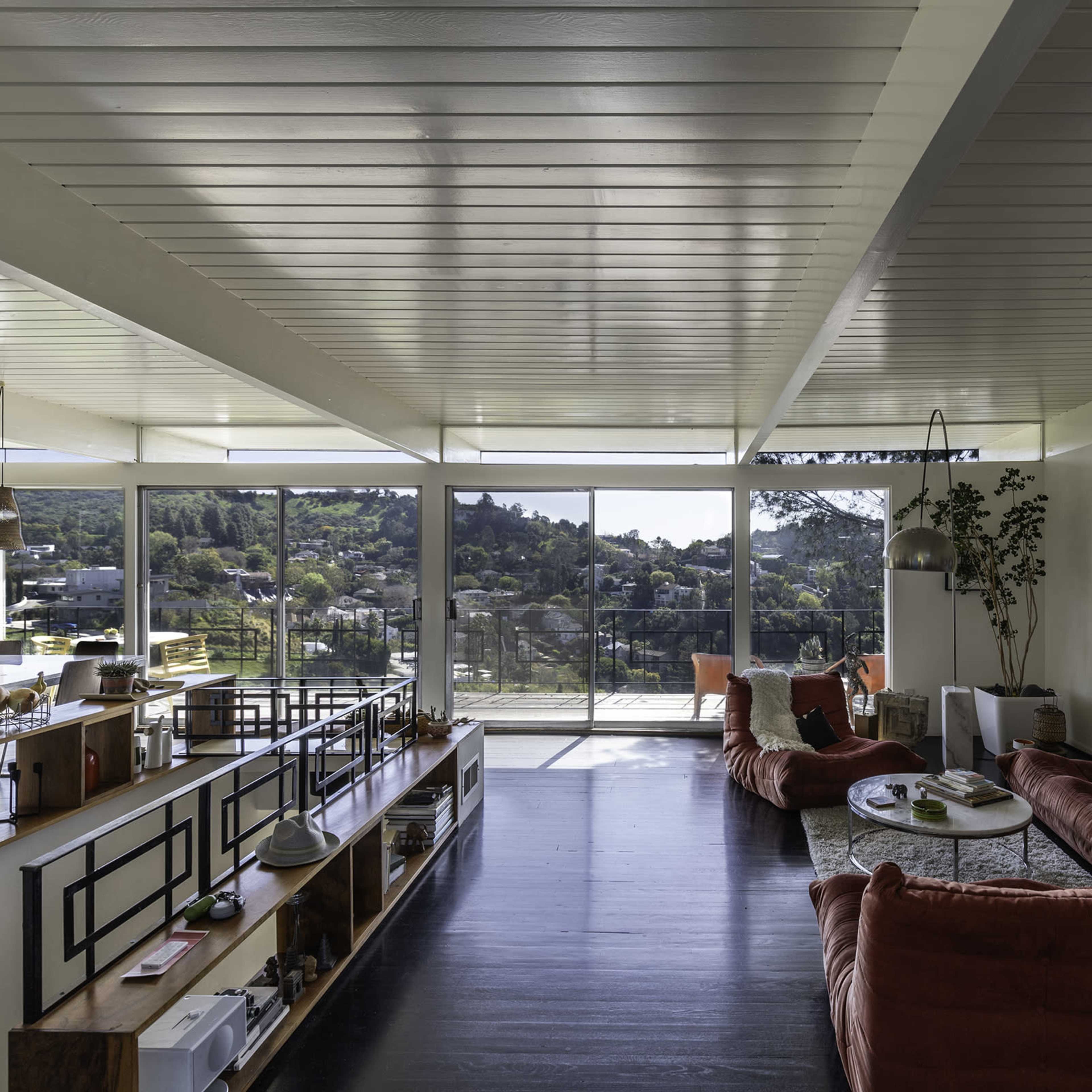 This interior features a spacious living area with large windows providing a view of the outdoors, surrounded by modern furnishings and decorative elements.