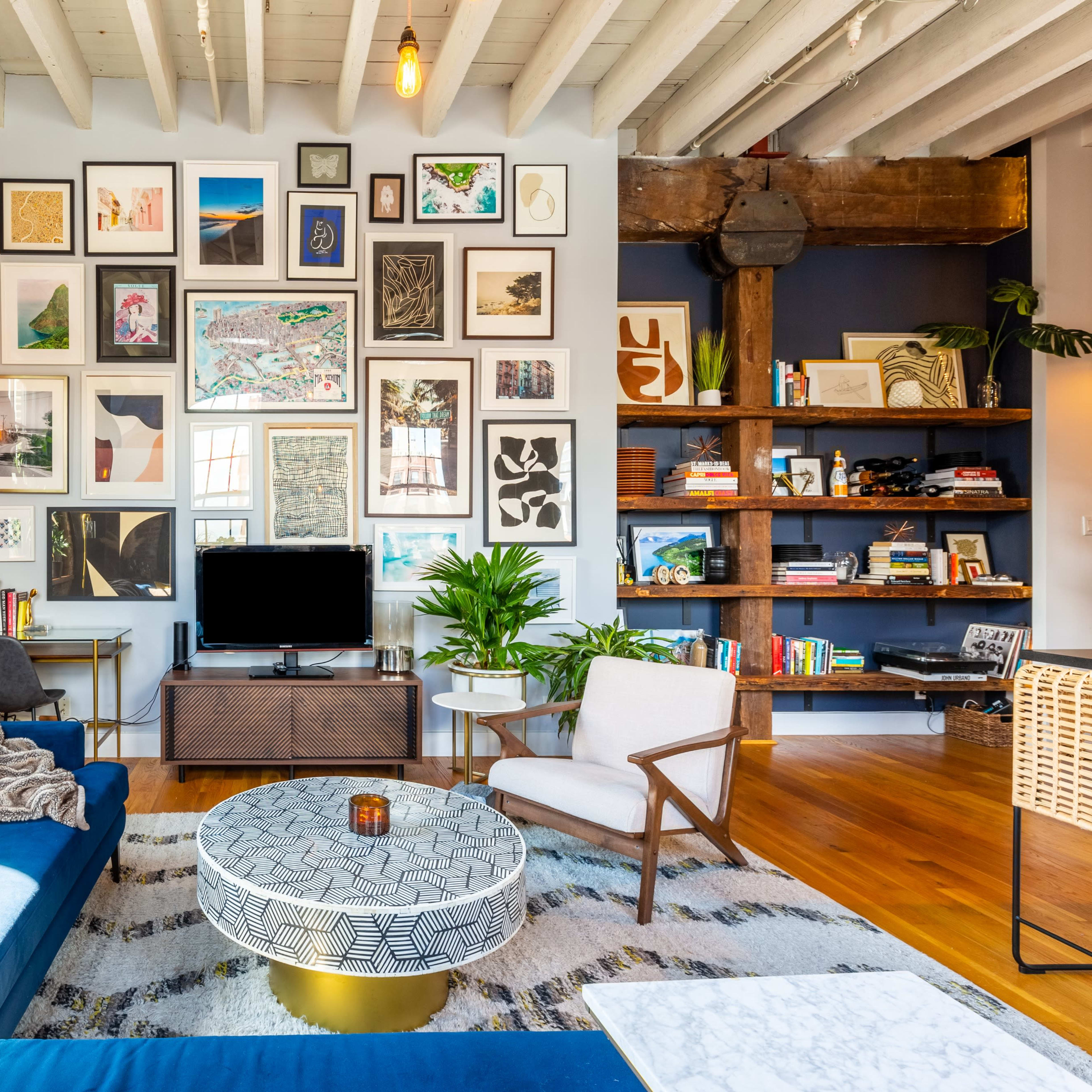 A stylish living room with a blue sofa, a round coffee table, a television cabinet, and a wall adorned with various framed artworks.