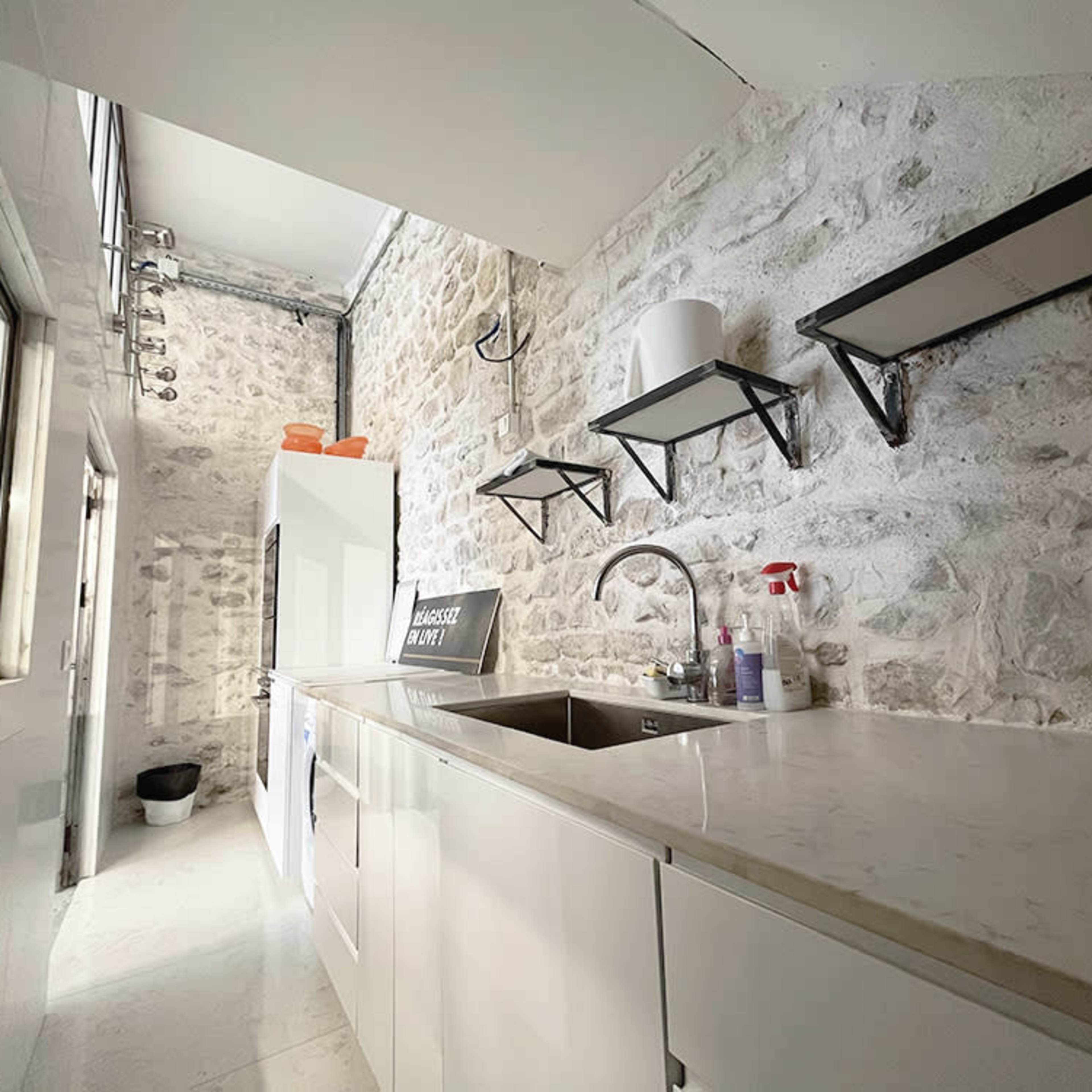 A narrow kitchen with stone walls, a white cabinet, and modern shelves above a sink.