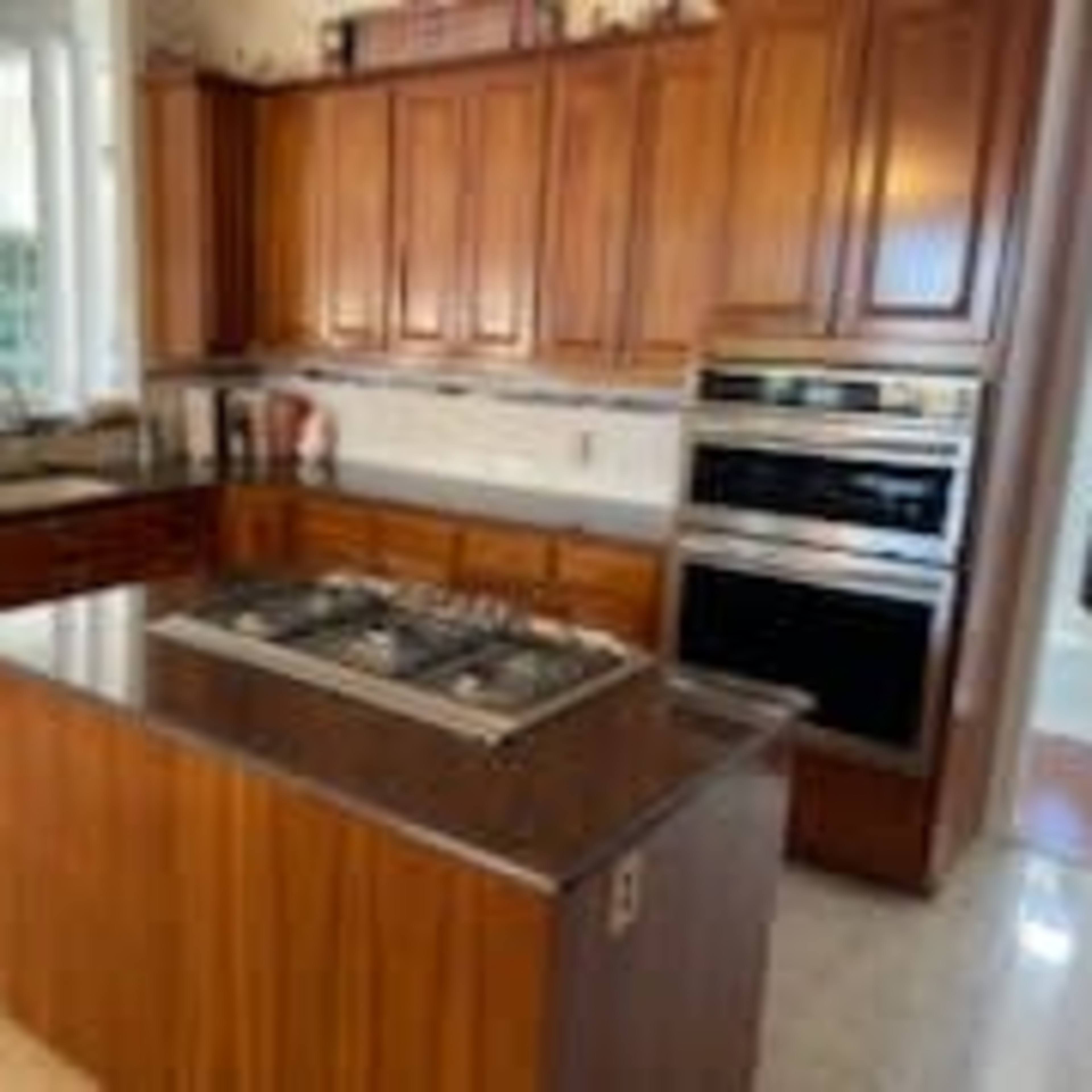 A modern kitchen with wooden cabinets, a center island featuring a gas cooktop, and built-in ovens.