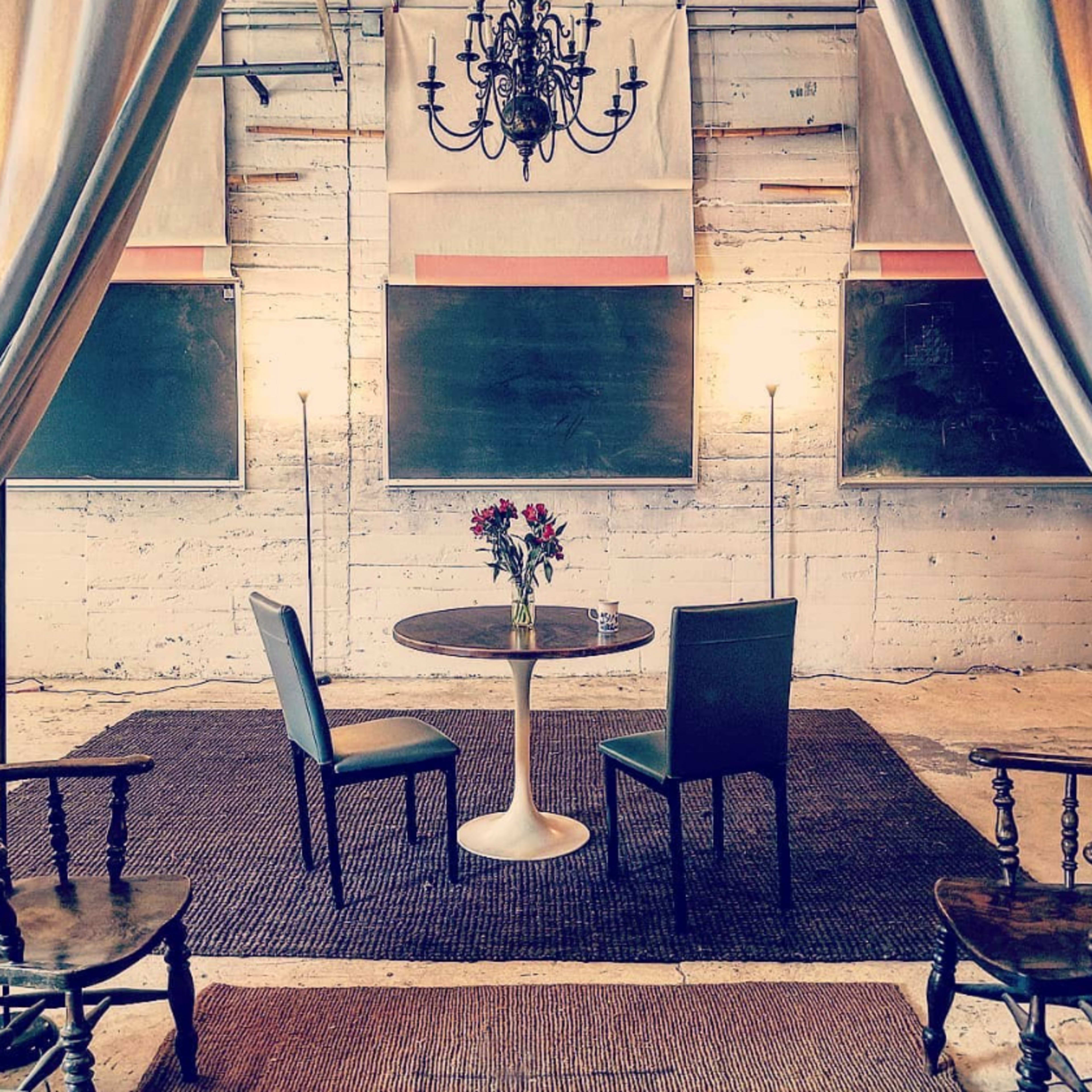 A round table with two chairs is positioned on a rug in a room featuring chalkboards and decorative lighting.