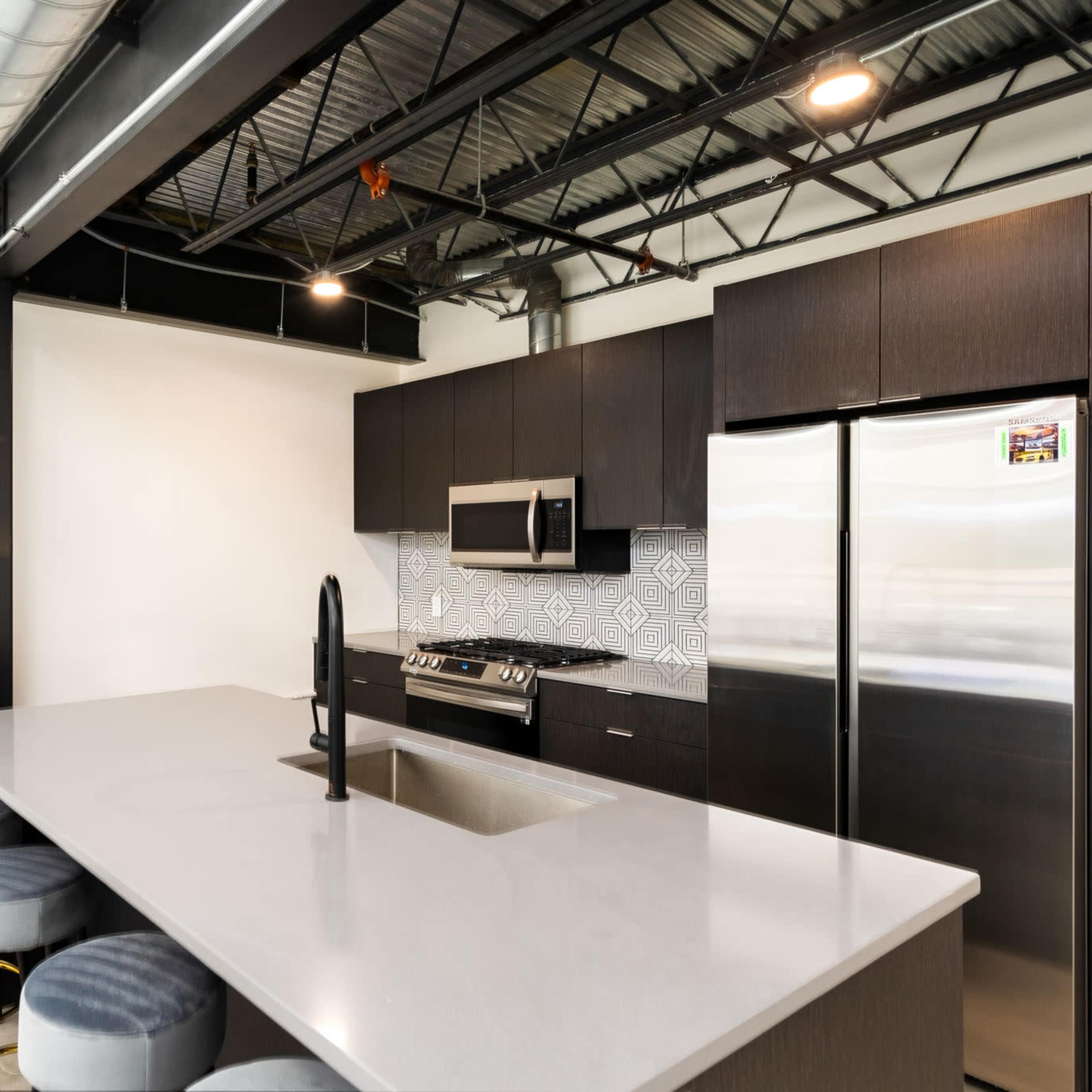 A modern kitchen with dark cabinetry, stainless steel appliances, a large island with a sink, and bar stools.