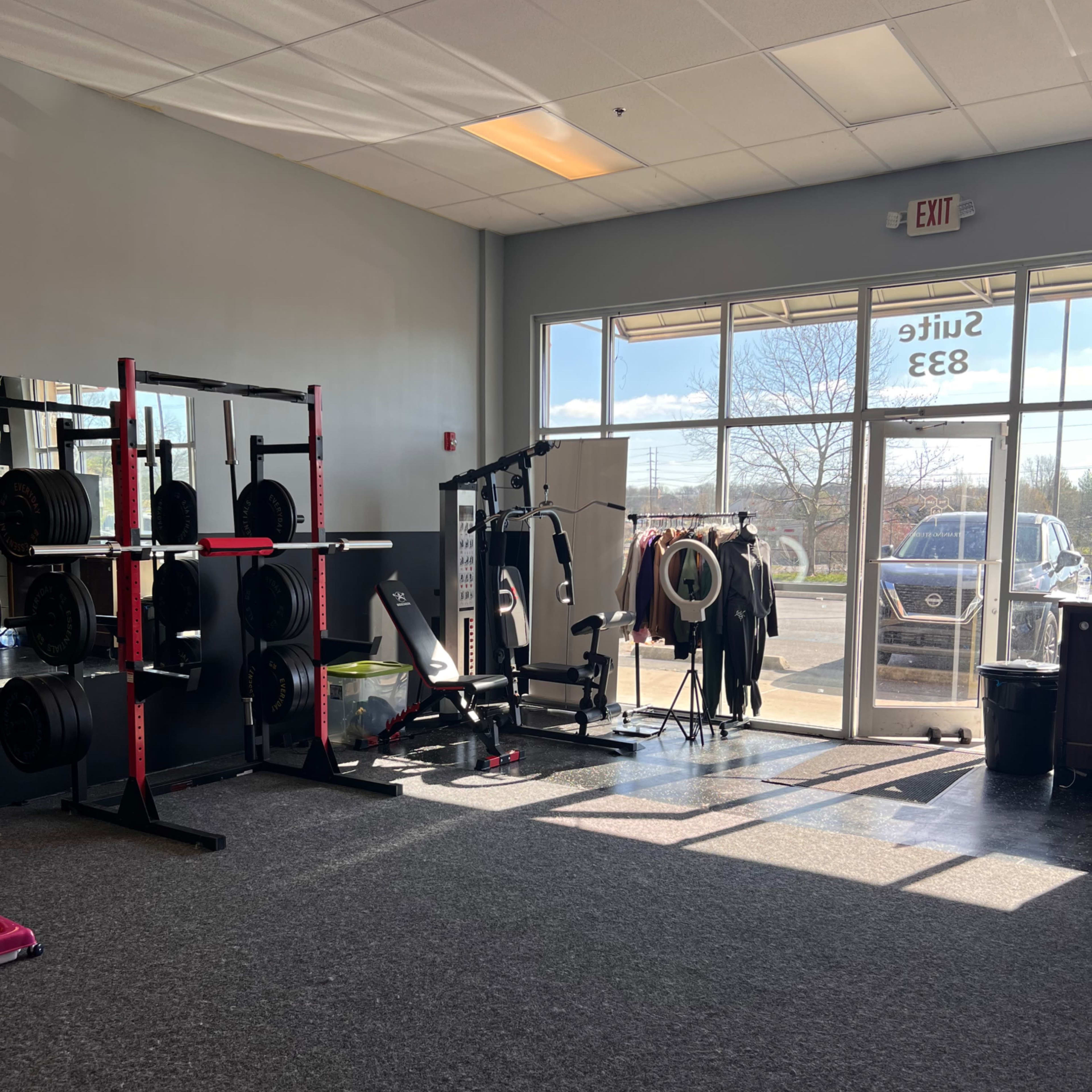 A gym interior with weightlifting equipment on one side and a large window offering outdoor views.
