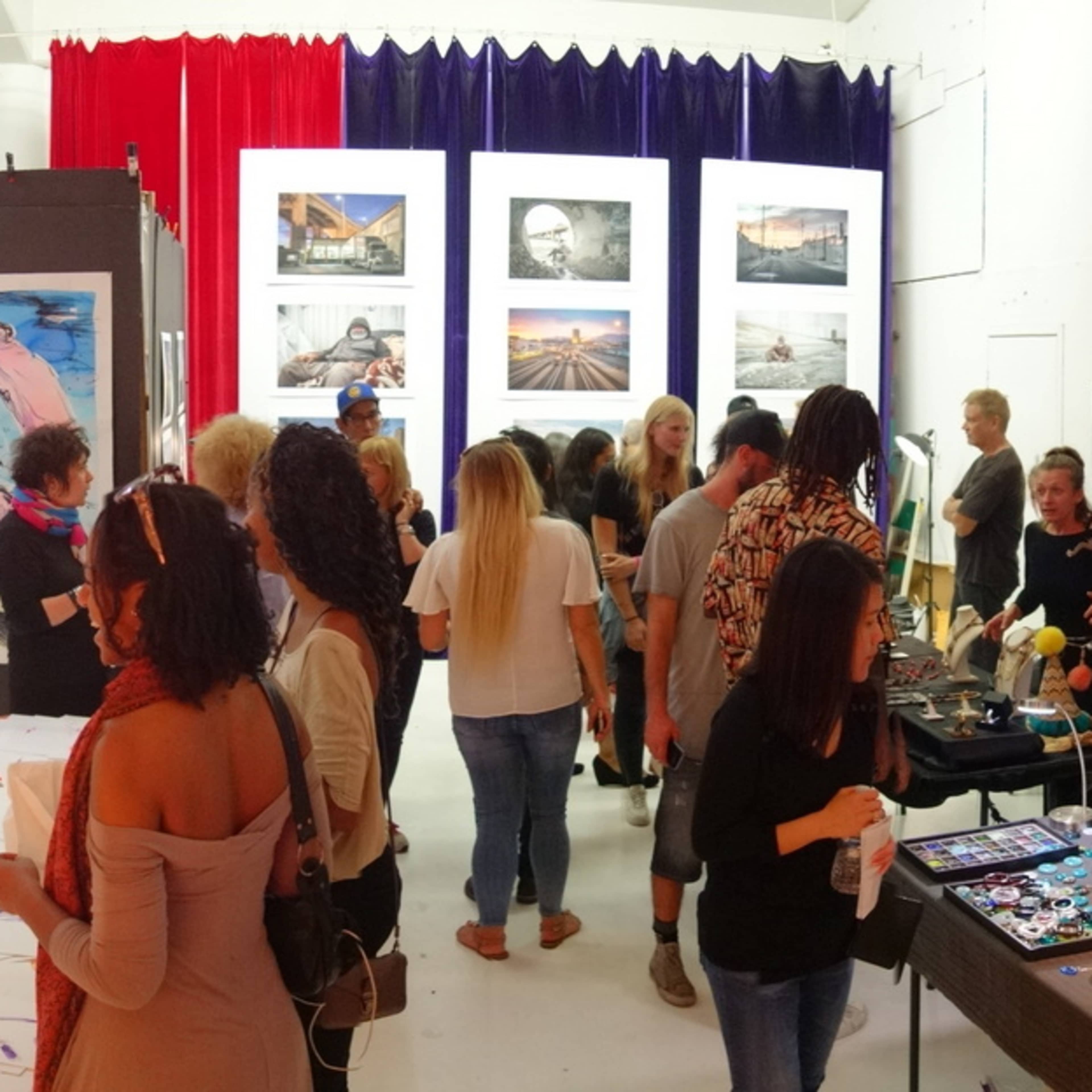 A crowd of people explores an art exhibition featuring various displays and artworks in a brightly lit space.