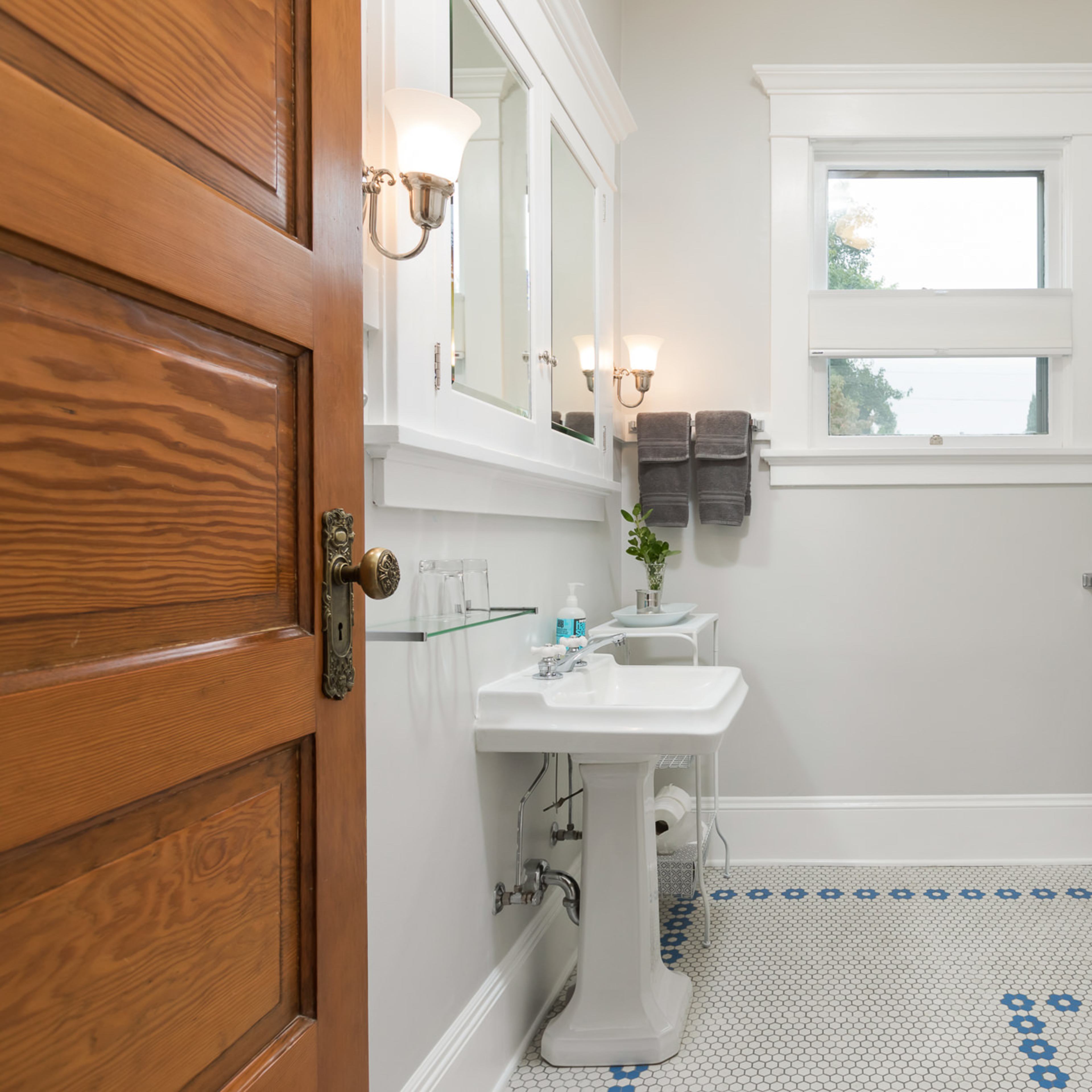A modern bathroom featuring a white shower curtain, a pedestal sink, and decorative tile flooring.