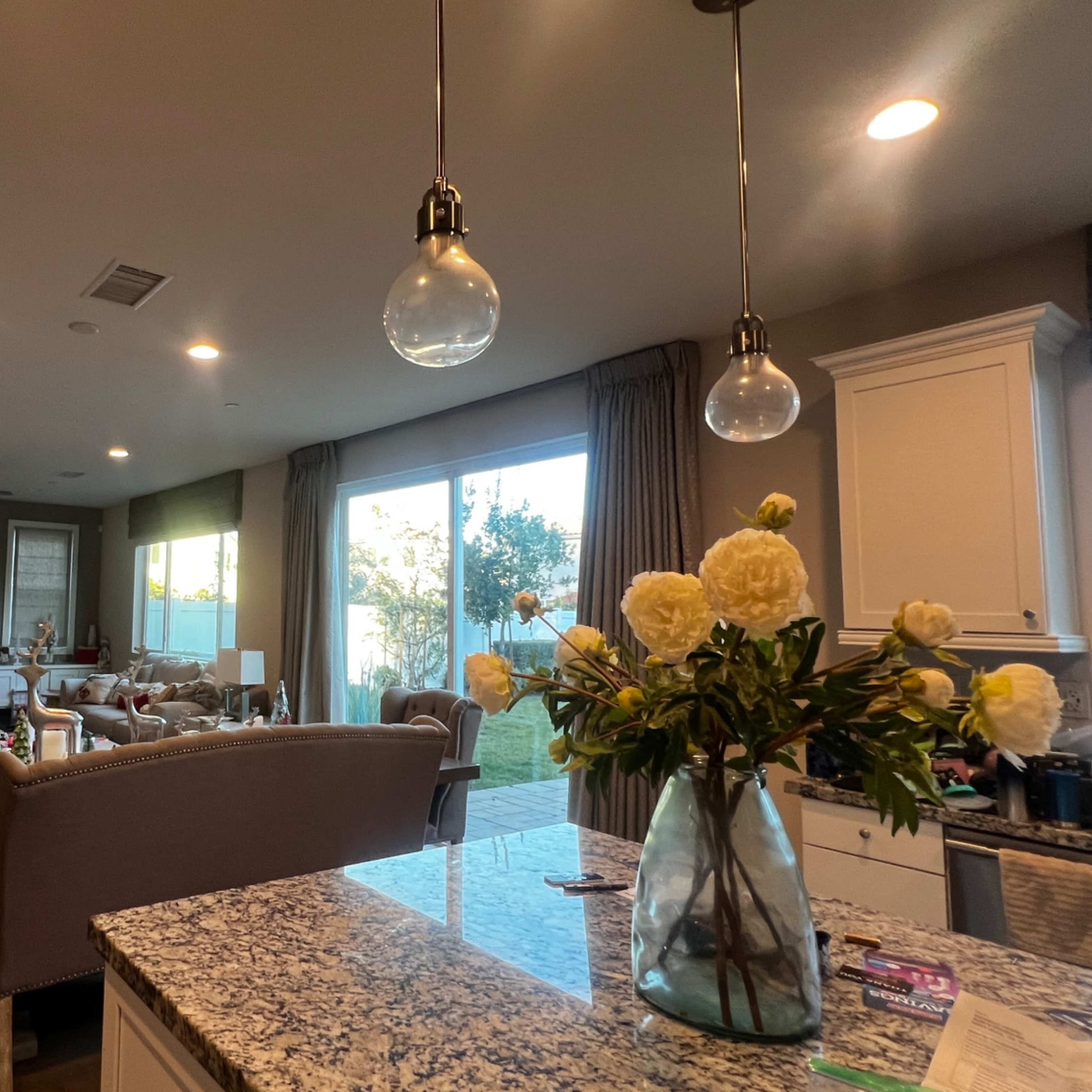 A modern living room and dining area with a Christmas tree, large windows, and a kitchen counter featuring a vase of flowers.