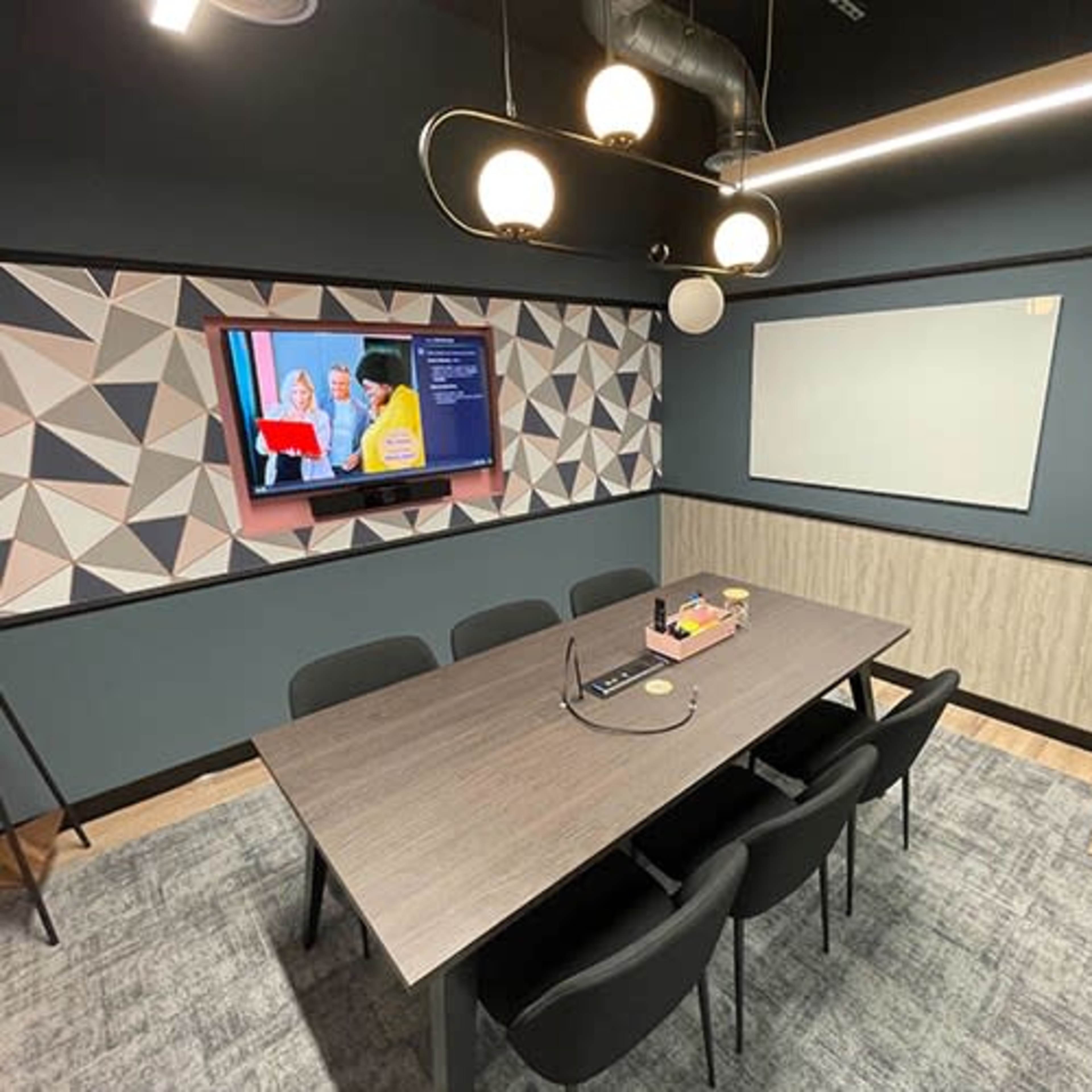 A modern conference room with a large table, black chairs, a television on the wall, and a whiteboard.