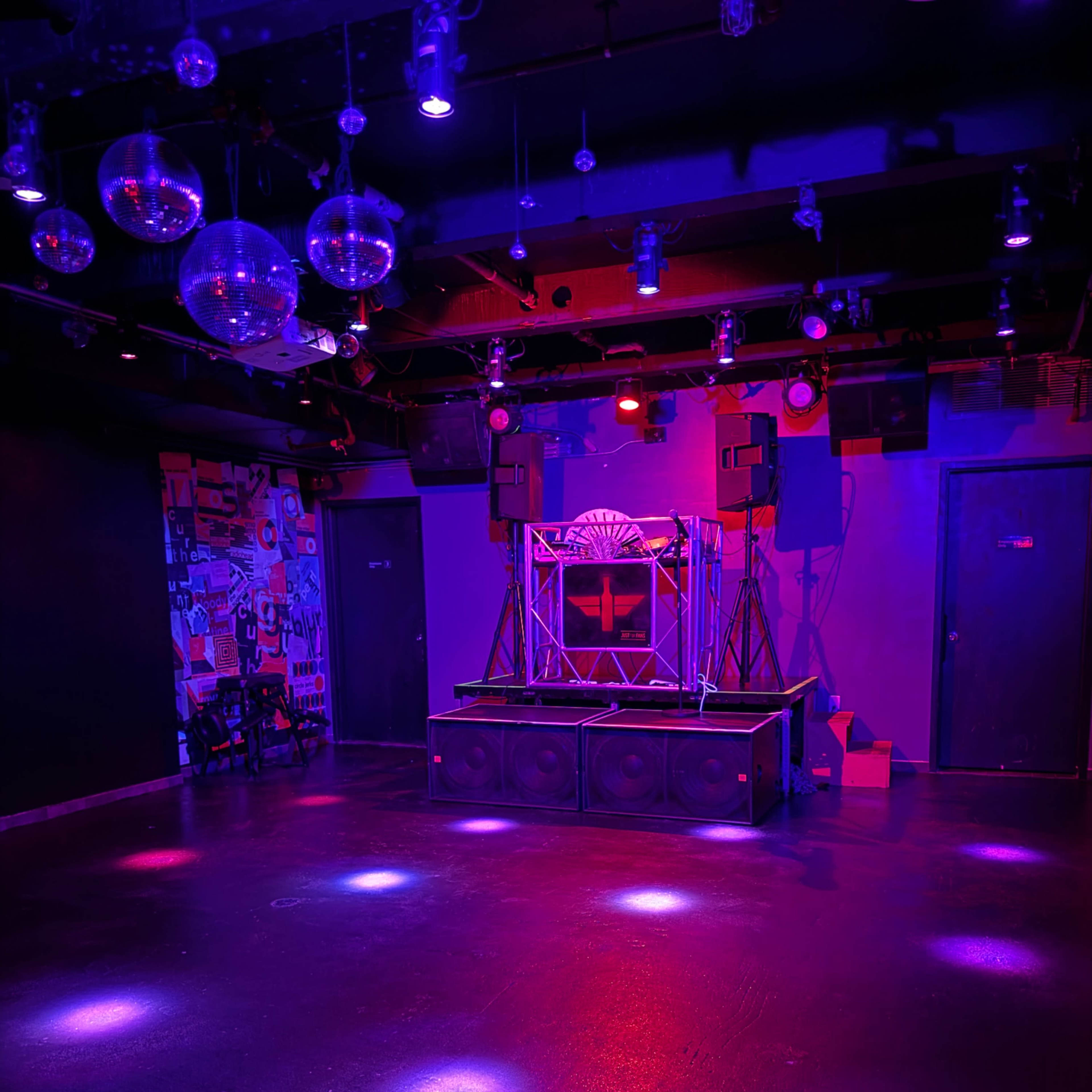 A dimly lit dance floor with a raised DJ platform surrounded by colorful lights and disco balls.