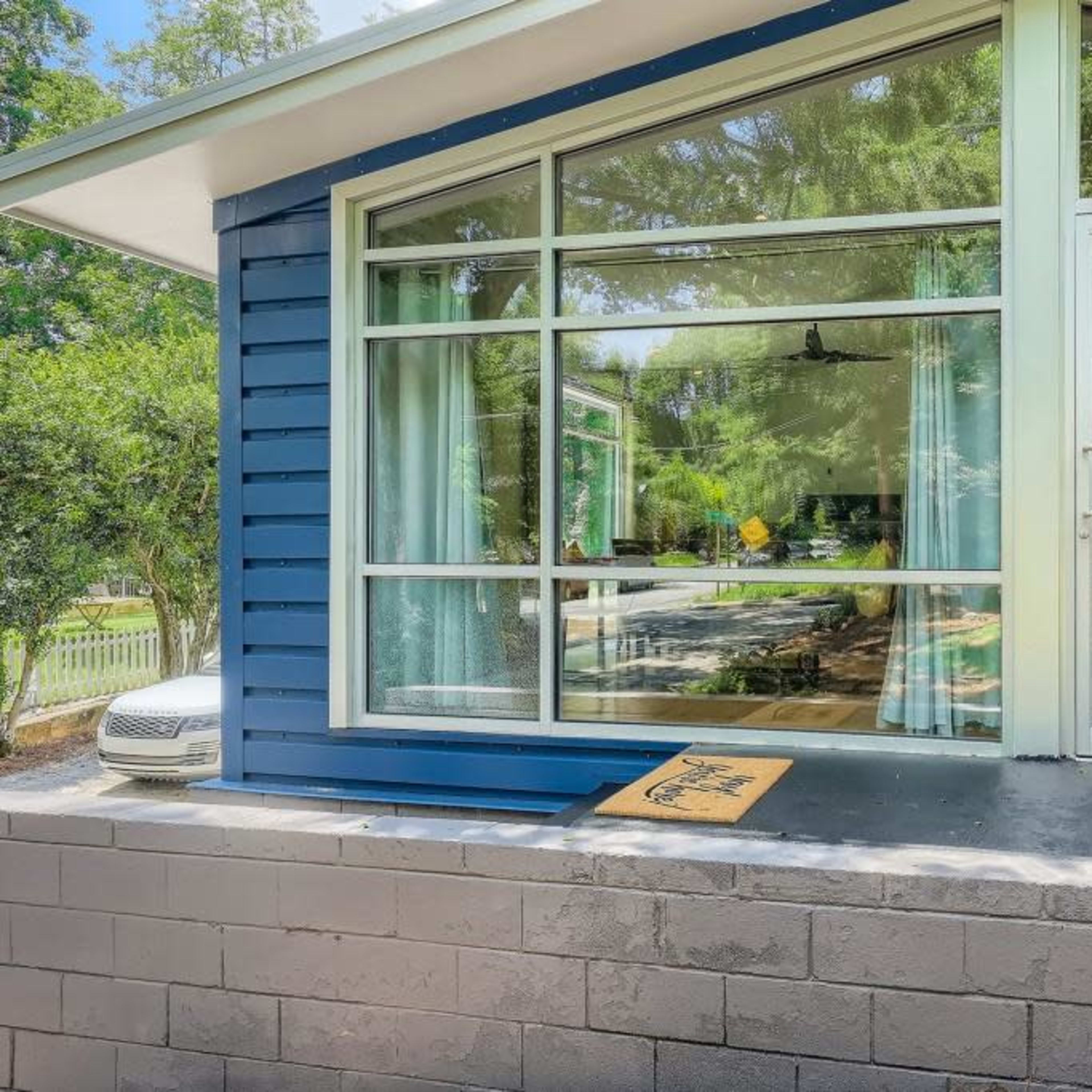 A modern house with large windows, a glass door, and a concrete wall, situated in a landscaped yard.