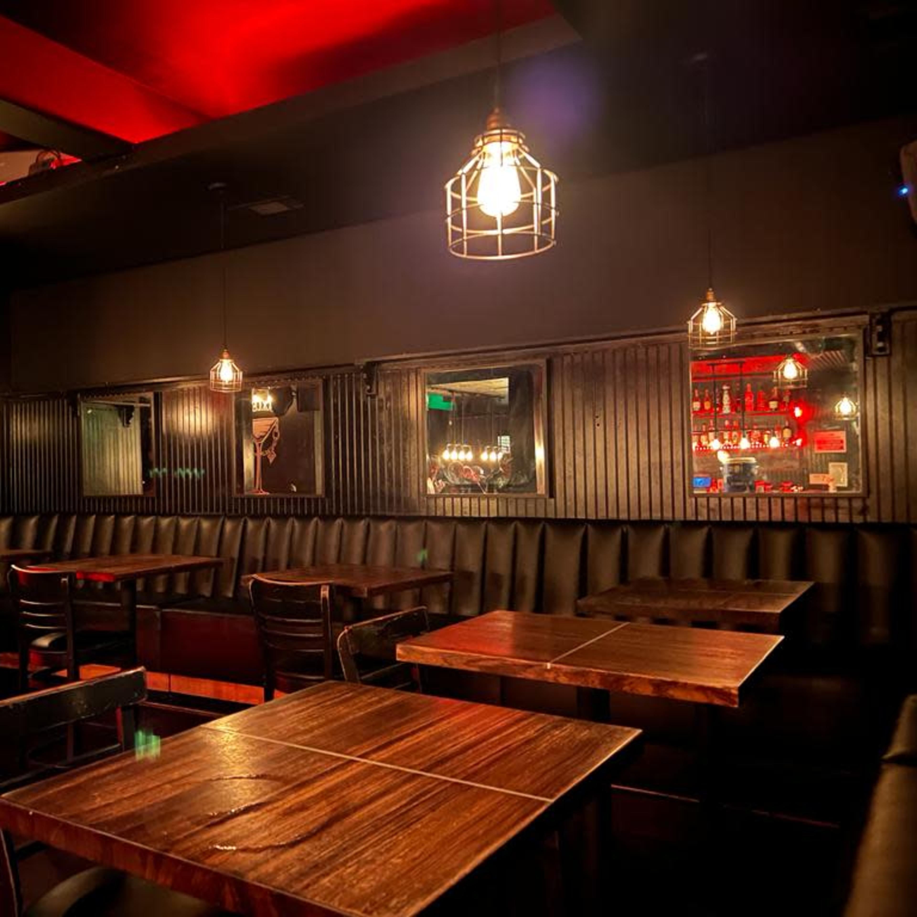 A dimly lit restaurant interior featuring wooden tables, black leather seating, and hanging pendant lights.