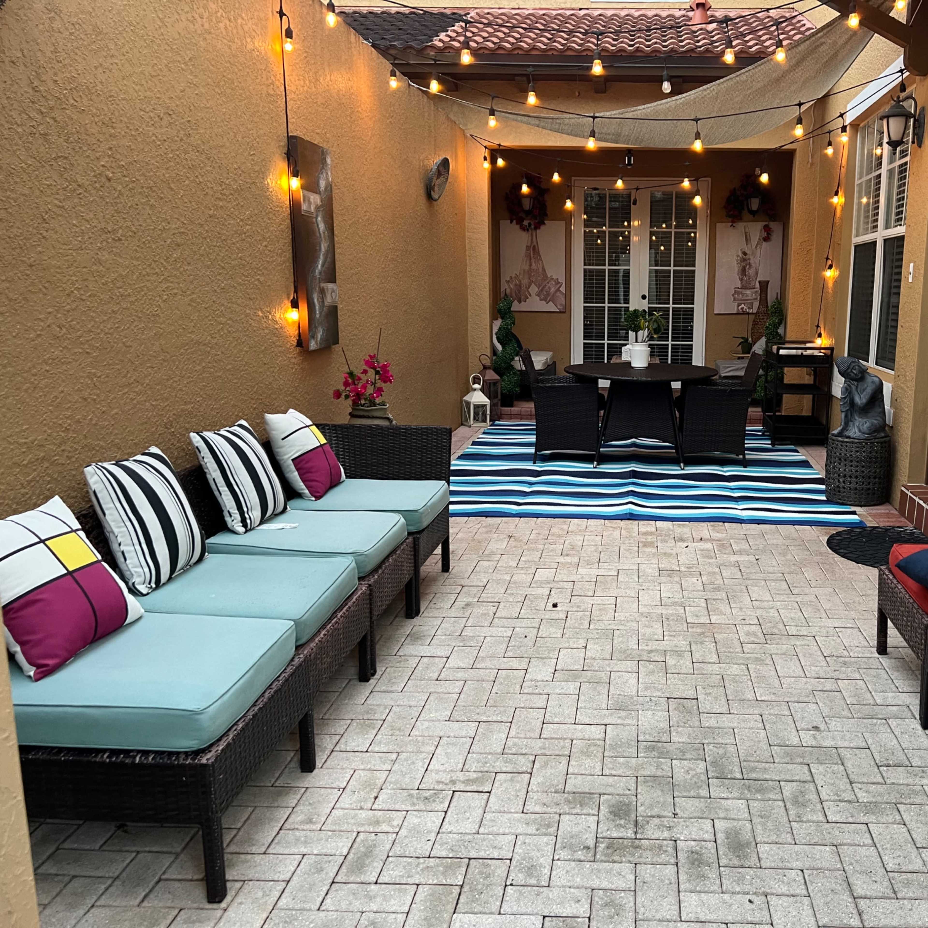 A patio area with several seating options, a dining table in the center, and decorative string lights overhead.