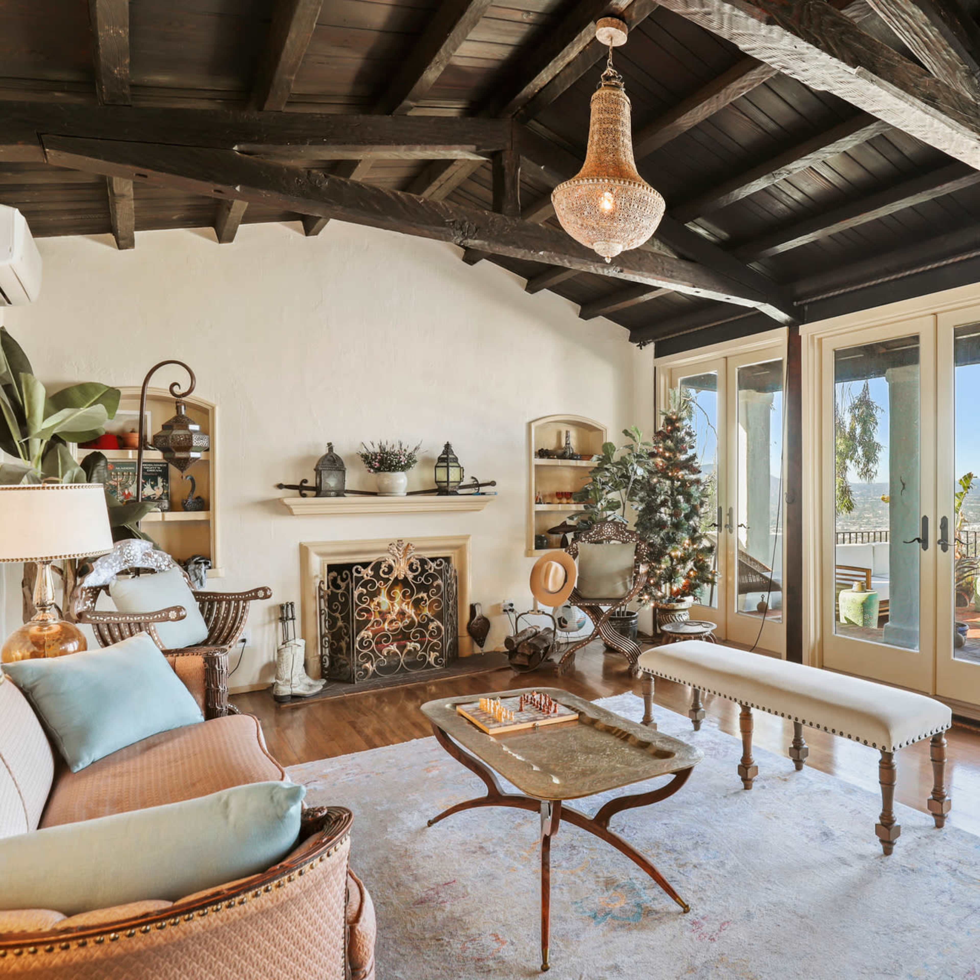 A cozy living room features a vintage sofa, a decorative fireplace, and large glass doors opening to a scenic view.