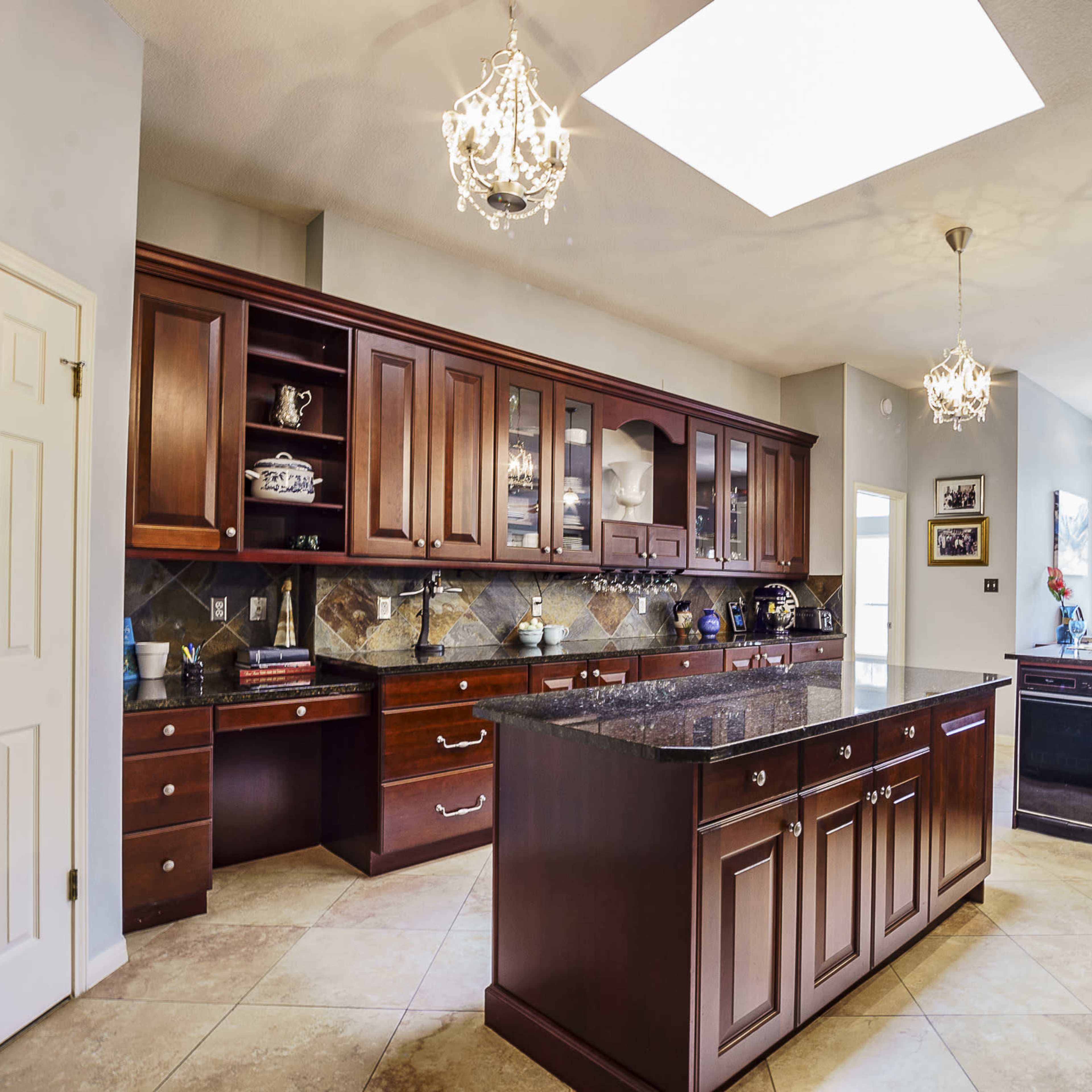 A spacious kitchen with wooden cabinetry, a large island with a granite countertop, and pendant lighting.