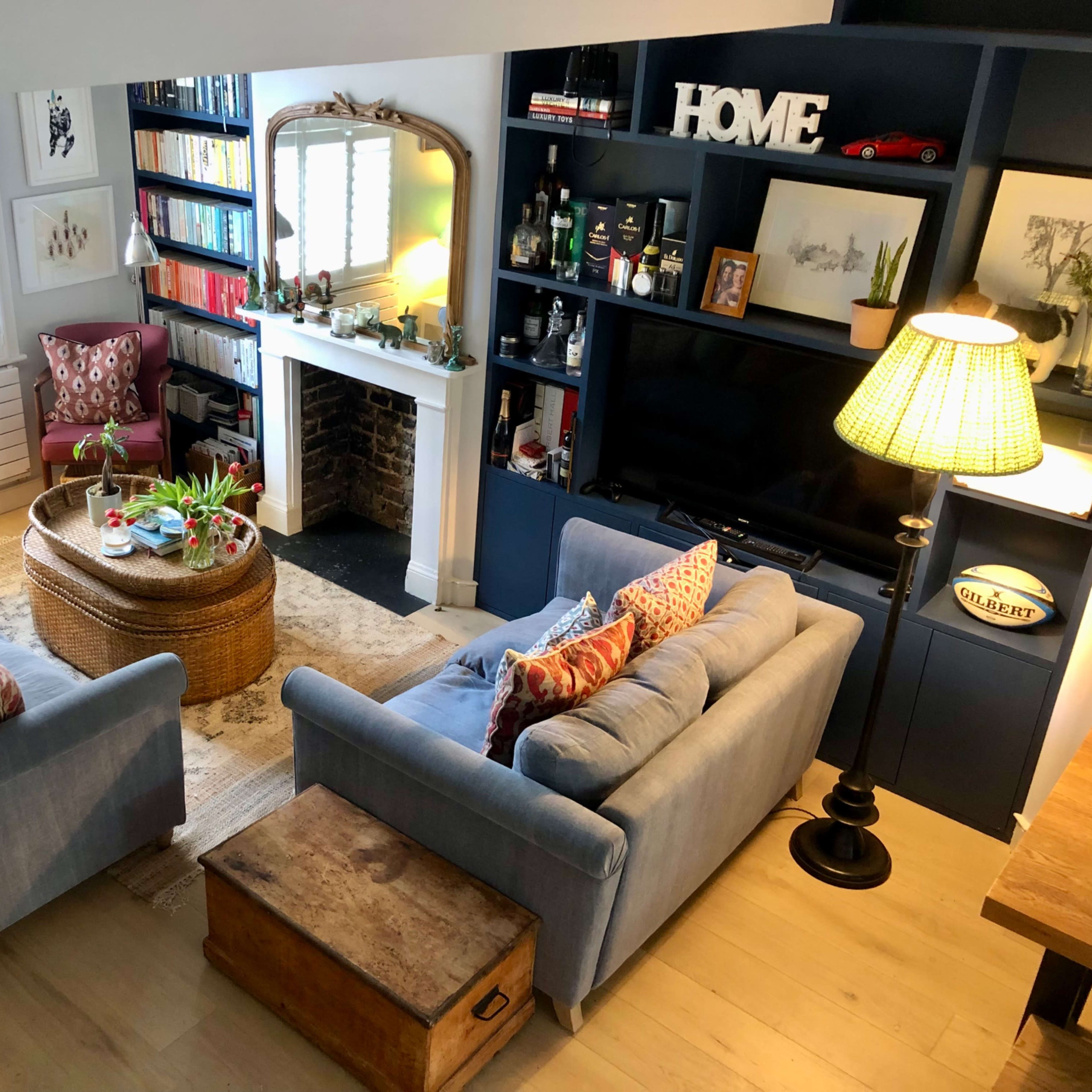 A cozy living room with two blue sofas facing a wicker coffee table, a fireplace surrounded by shelves, and a wall-mounted television.