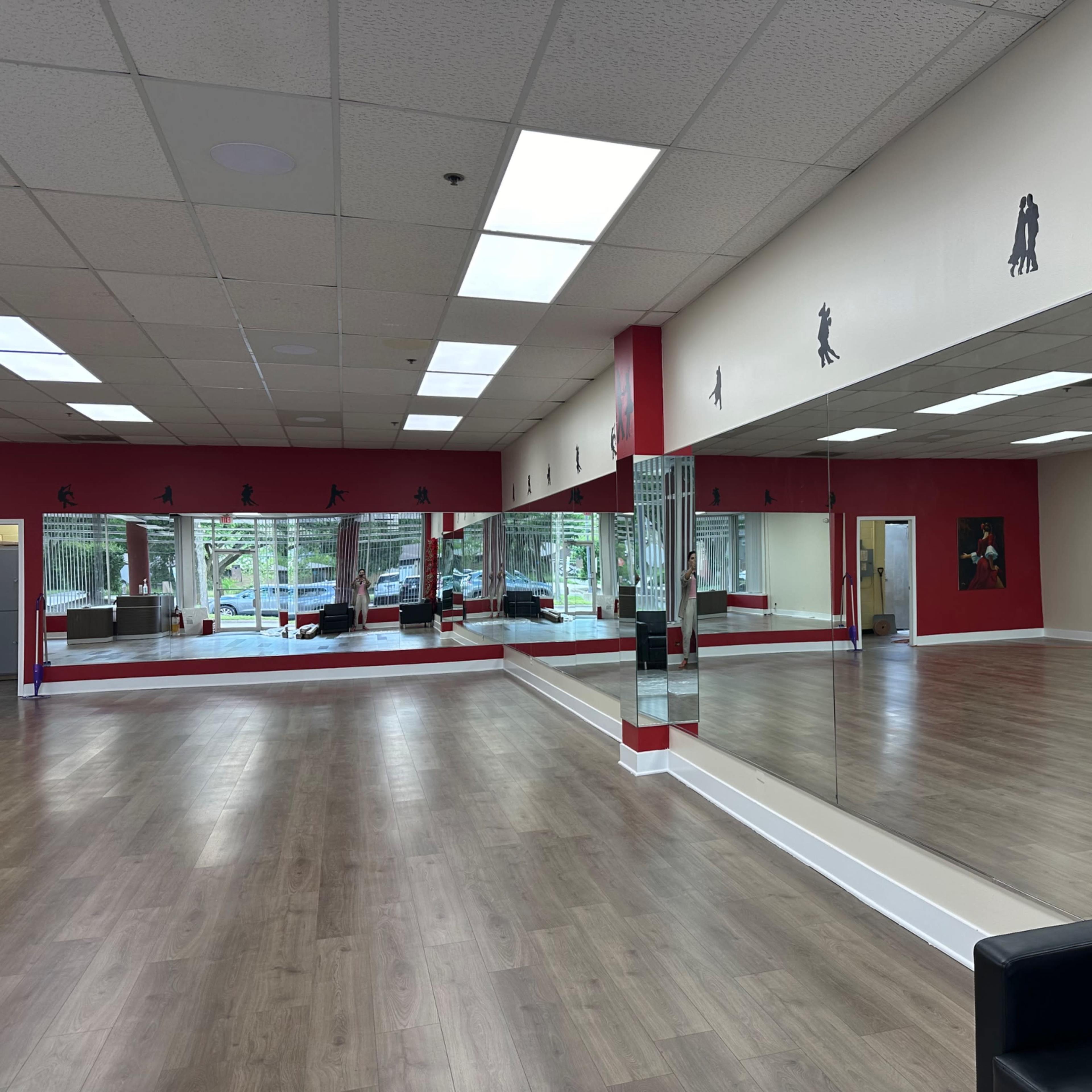 A spacious dance studio with large mirrors, wooden flooring, and a decorative wall featuring silhouettes of dancers.