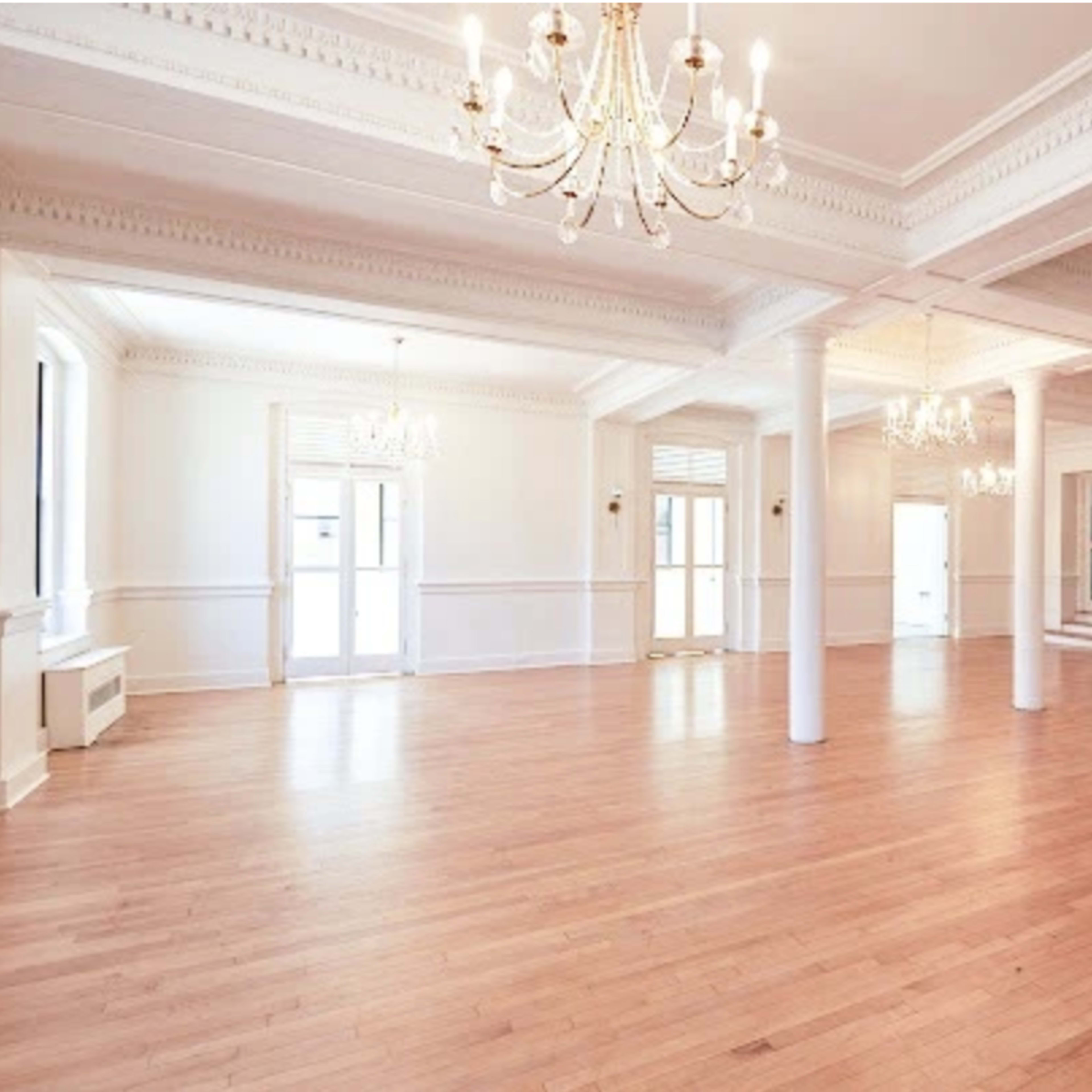 A spacious, well-lit interior room with wooden floors and multiple chandeliers.