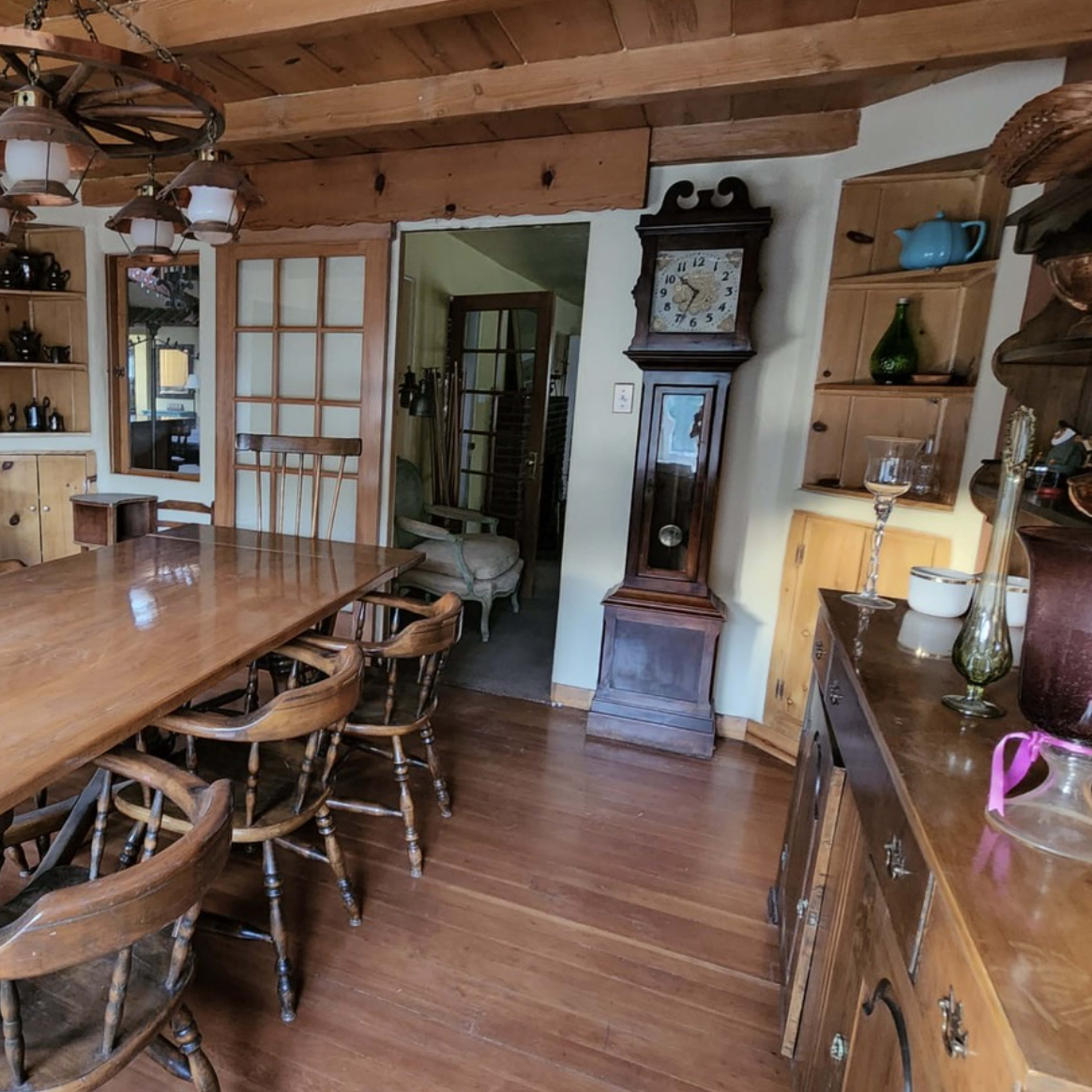 A rustic dining area with a large wooden table surrounded by chairs, wooden cabinetry, and a clock against the wall.