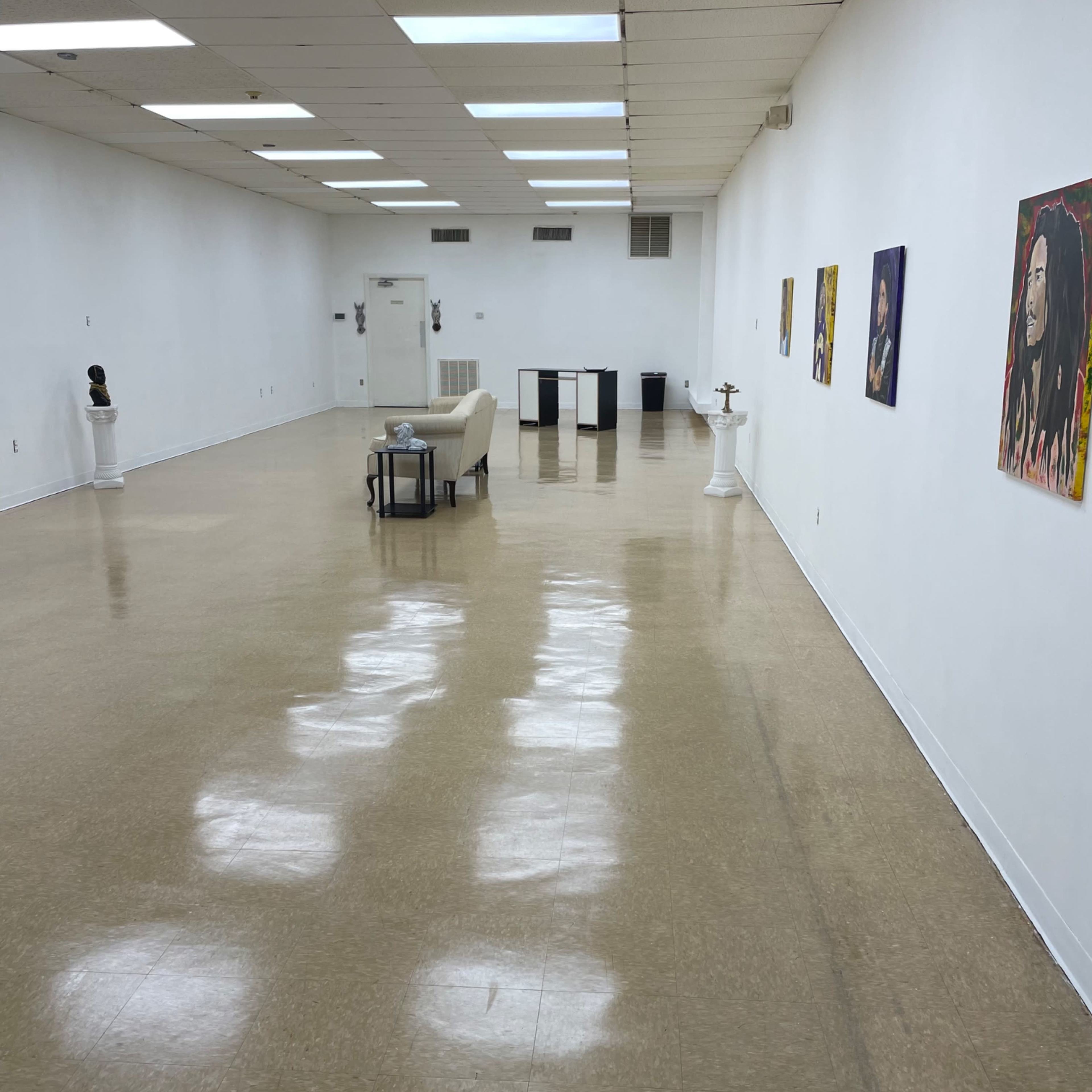 A spacious, empty gallery with polished floors, white walls, and a few pieces of art displayed.
