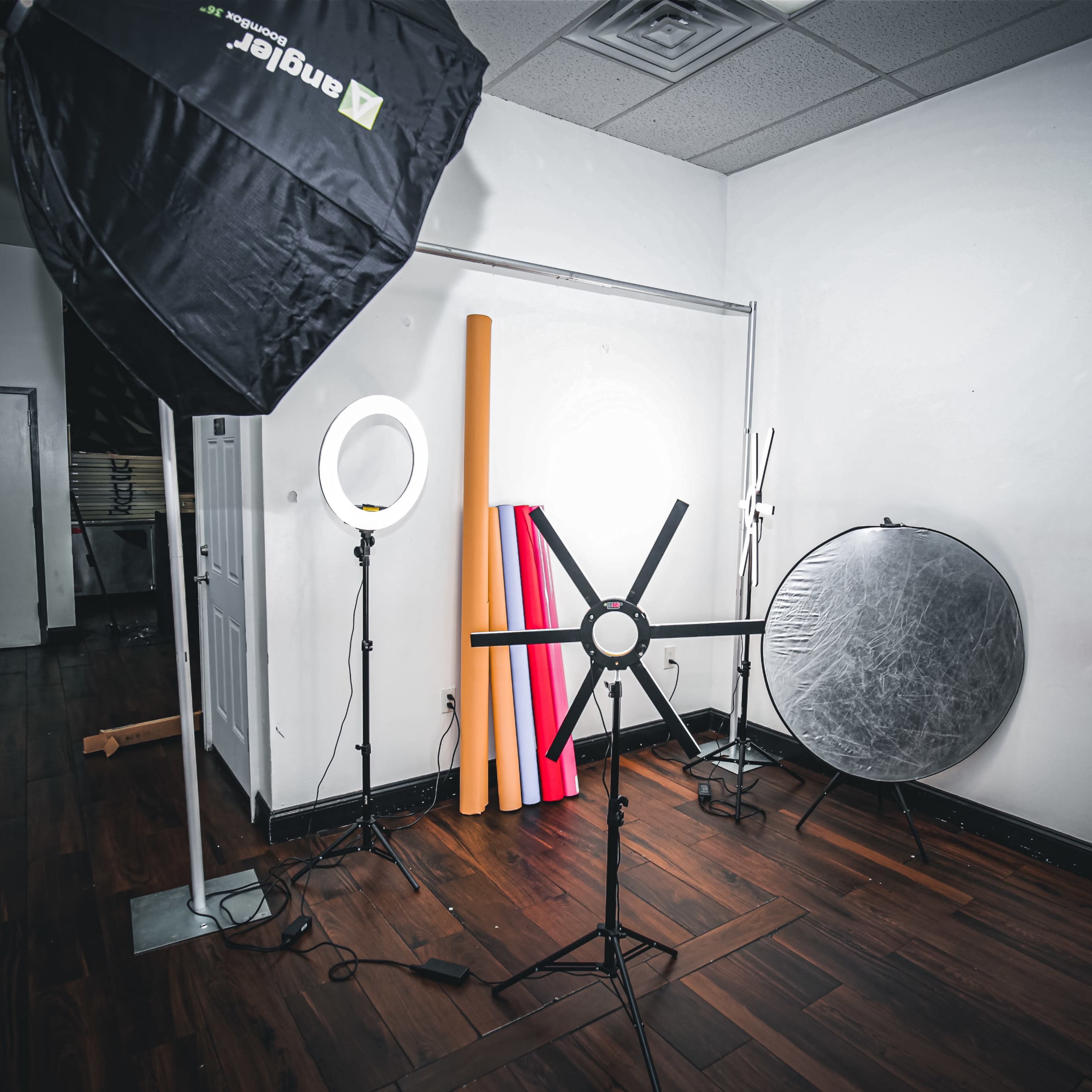 A photography studio setup with various lighting equipment and backdrops arranged against a white wall.