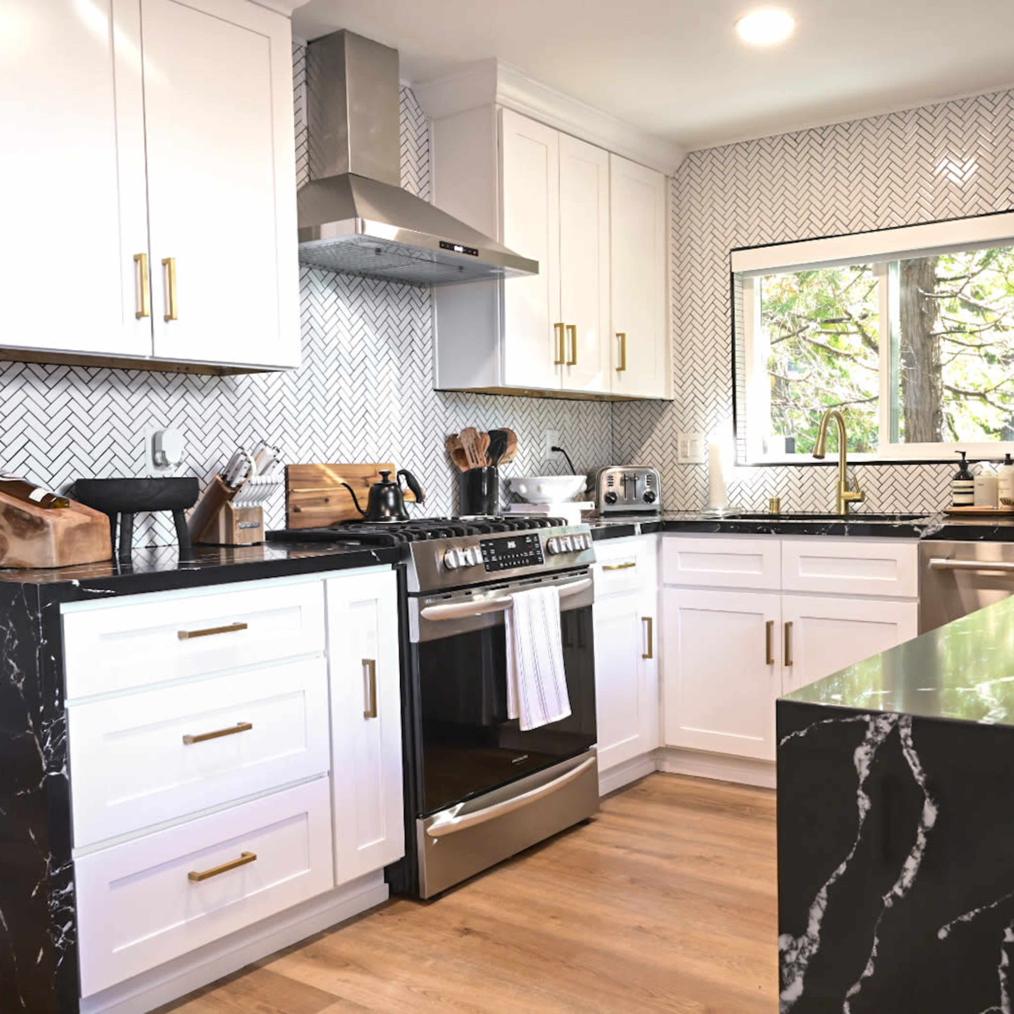 A modern kitchen features white cabinets, a black marble countertop, stainless steel appliances, and a window that provides natural light.