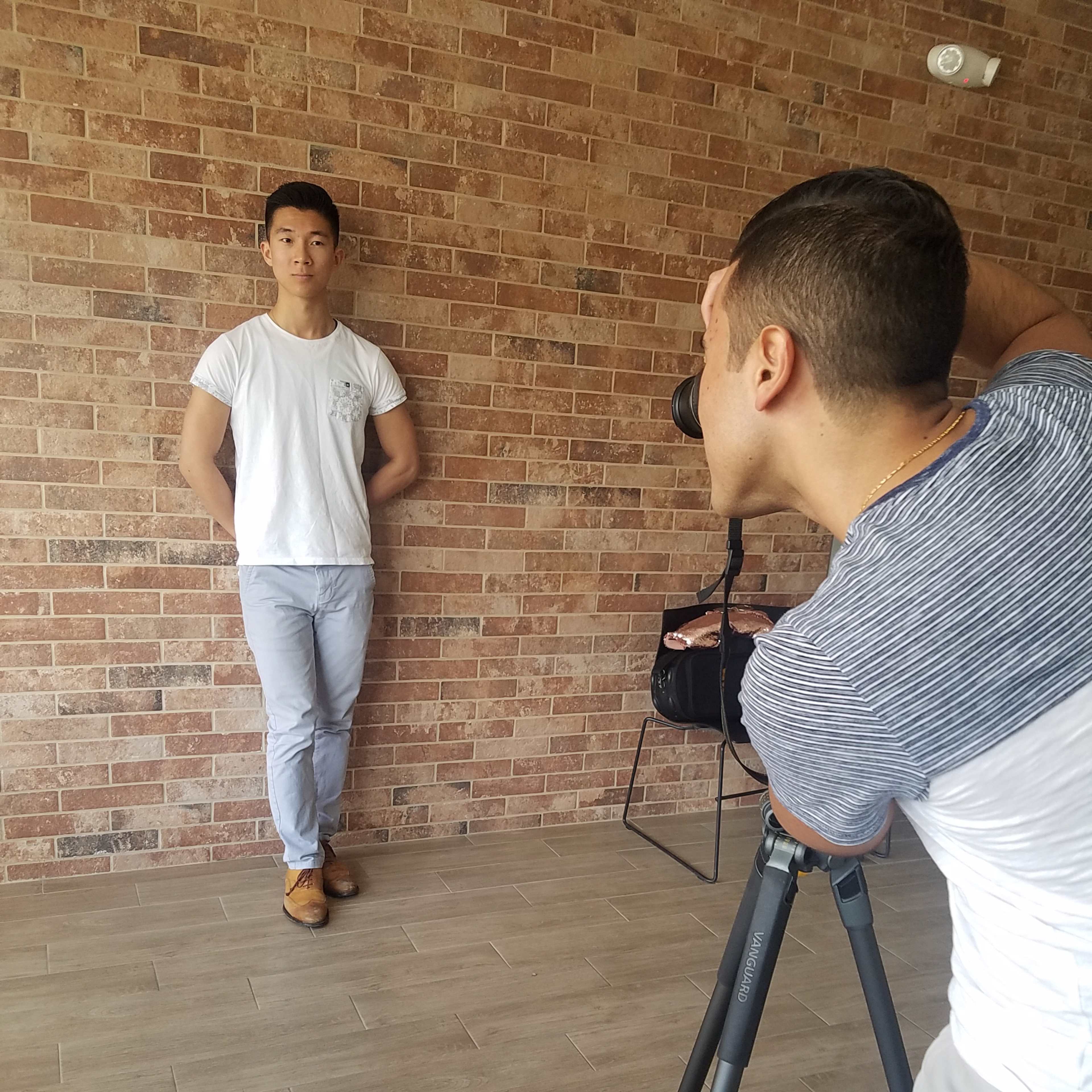 A photographer is capturing a portrait of a person standing against a brick wall.
