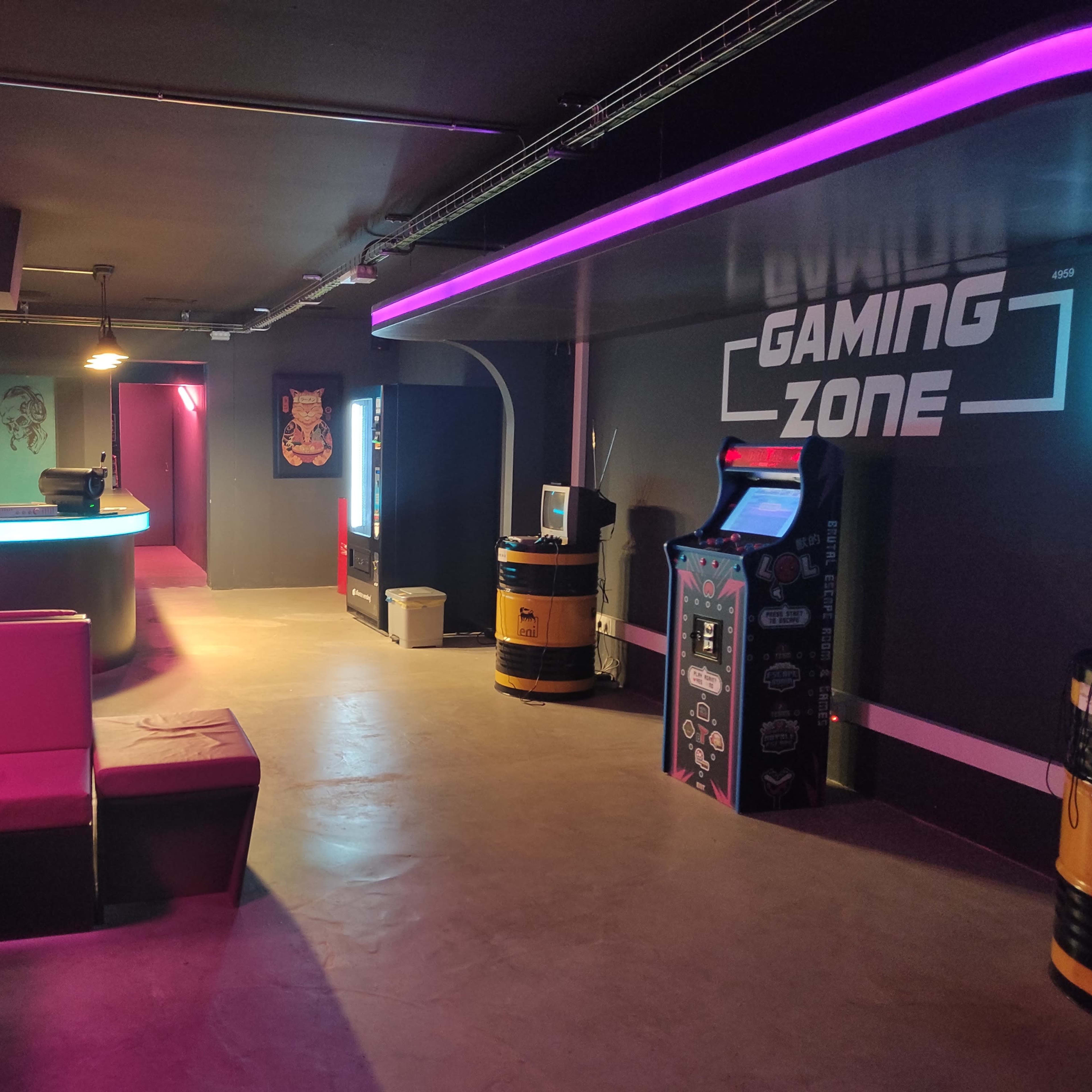 A dimly lit gaming zone with neon lights, featuring seating areas, vending machines, and arcade cabinets.