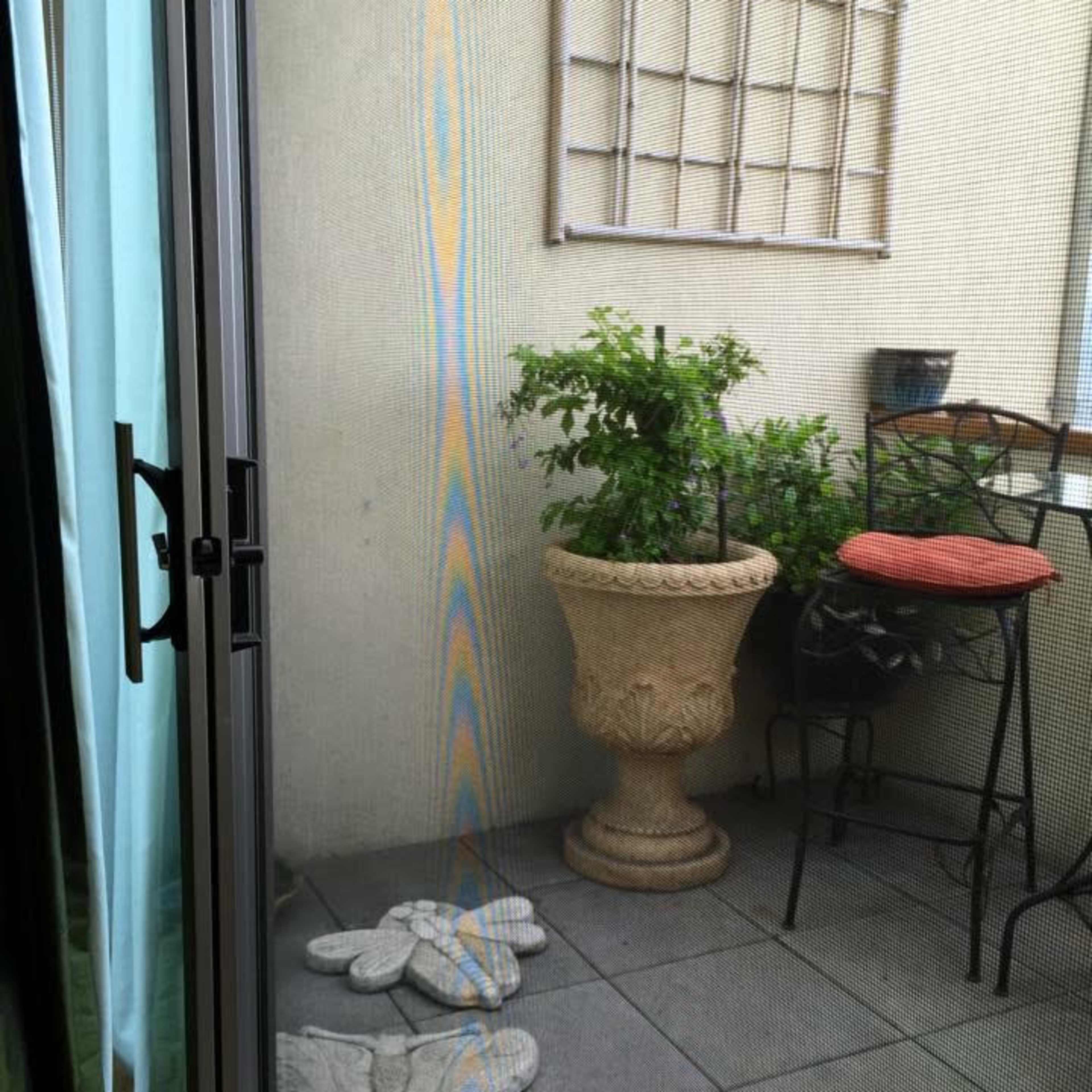 A small patio area with a potted plant, a chair with a cushion, and two stone figures on the tiled floor.