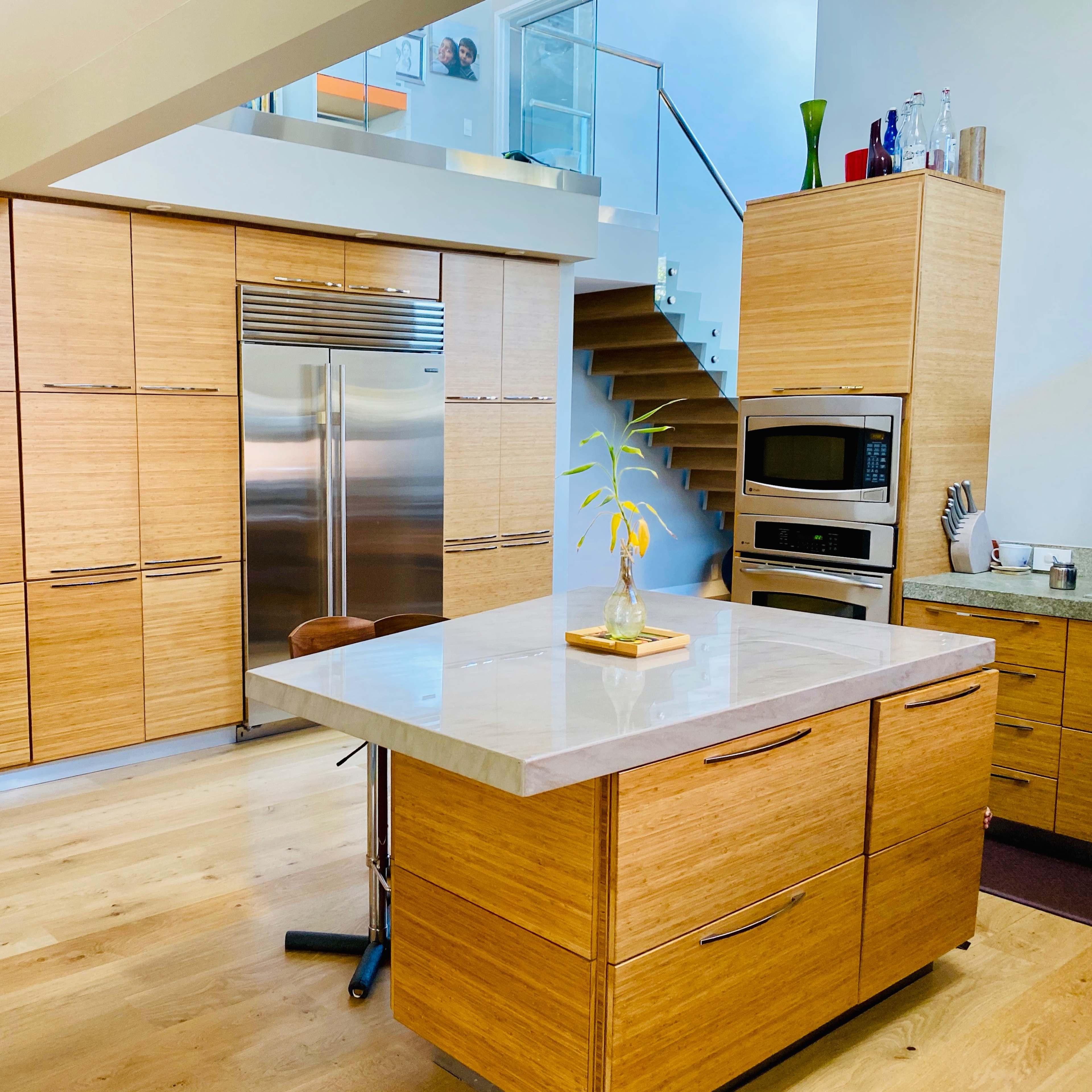 A modern kitchen with wooden cabinetry, a stainless steel refrigerator, and a central island topped with a light-colored stone surface.