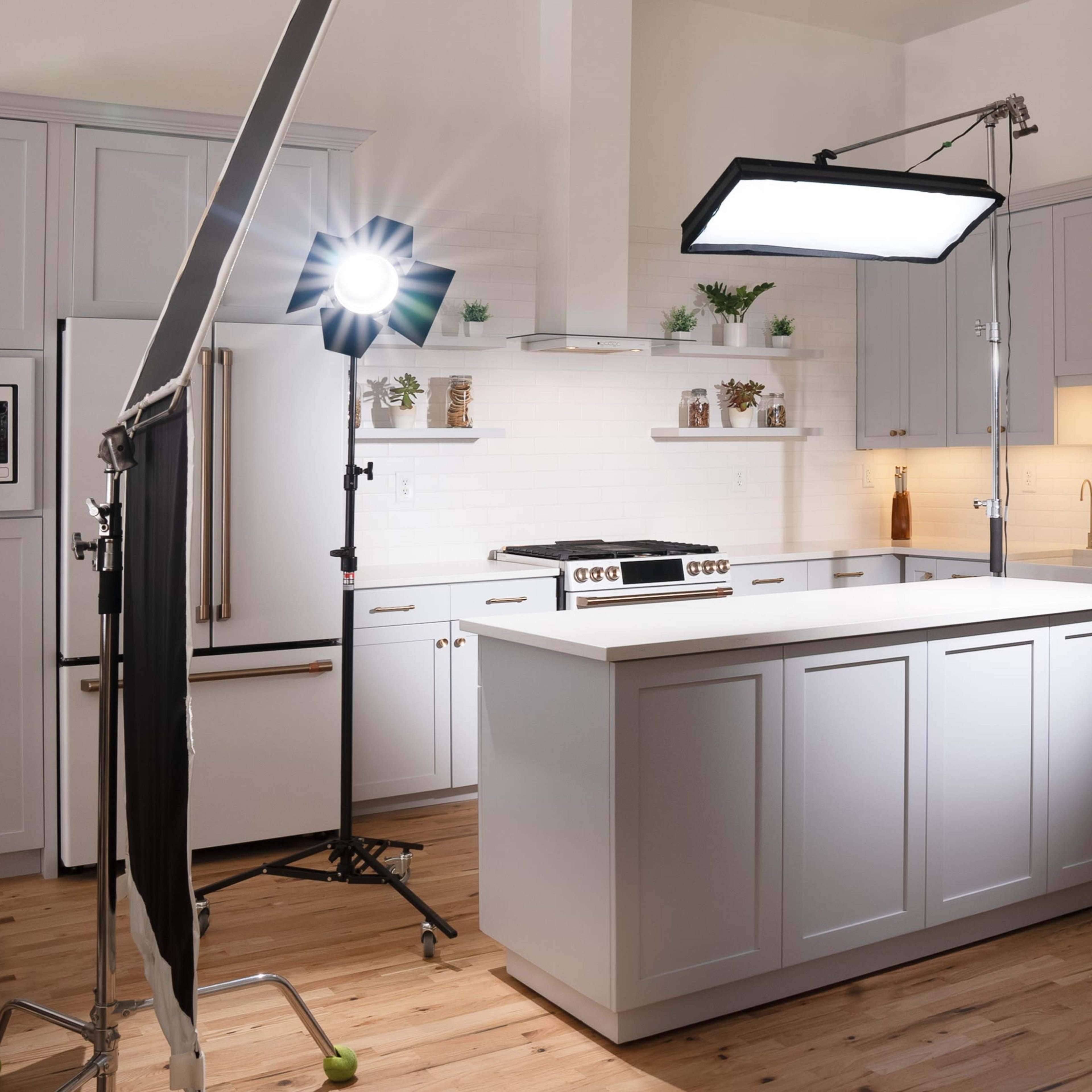 A modern kitchen is set up for a photoshoot with bright lights and equipment positioned around a central island.