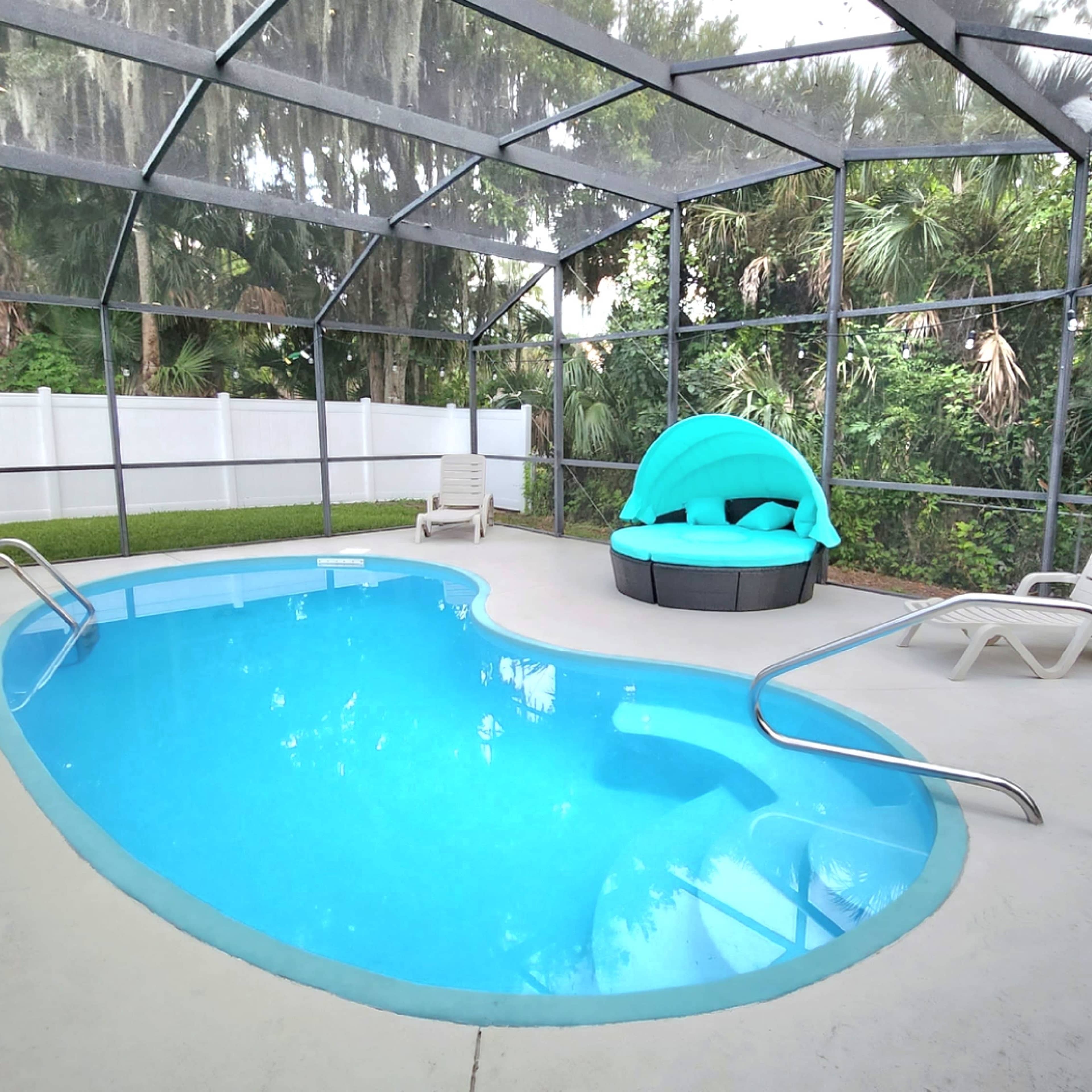 A screened-in pool area featuring a kidney-shaped pool, a curved seating area with bright blue cushions, and several lounge chairs beside the water.