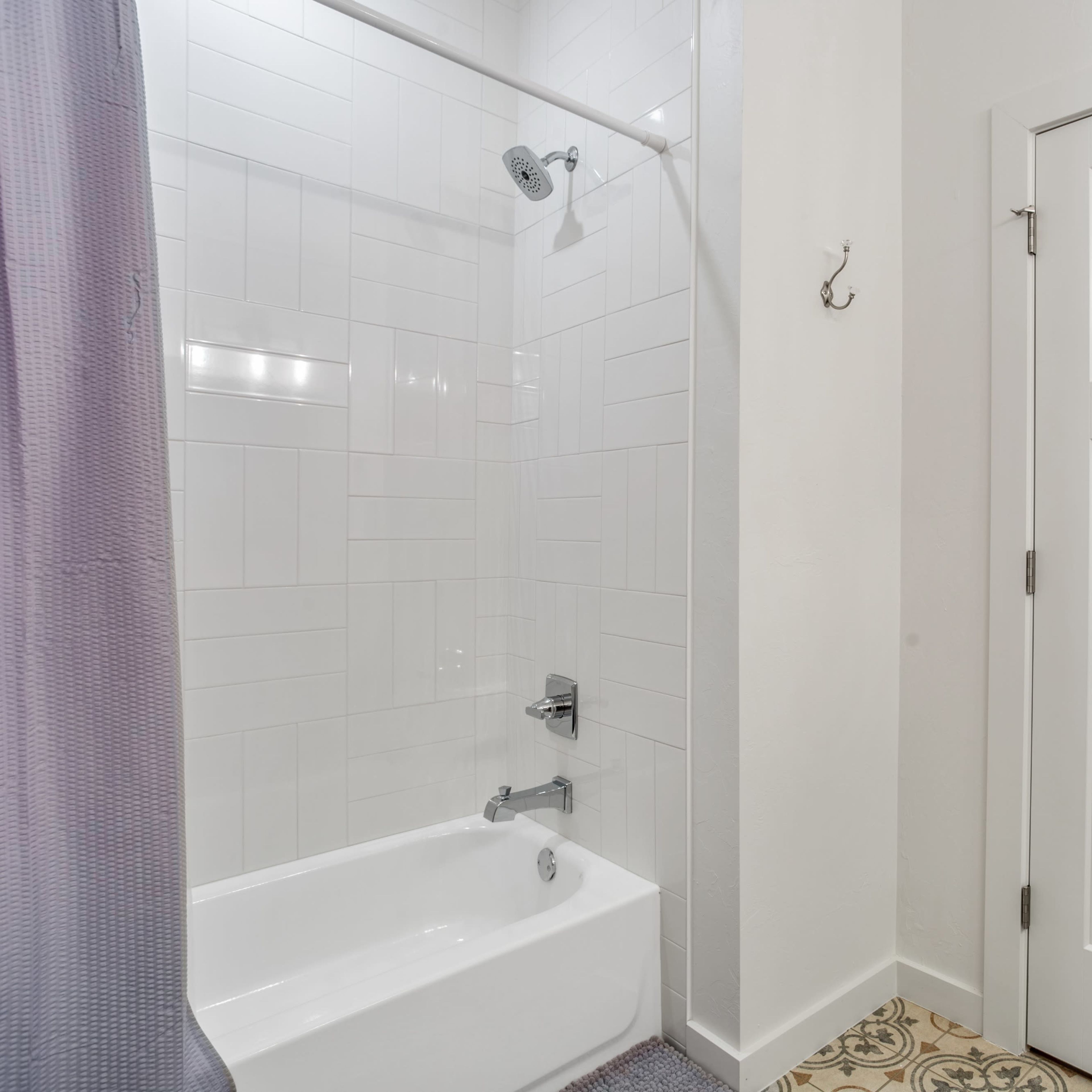 A bathroom featuring a bathtub with a shower, white tiled walls, and a door on the right side.
