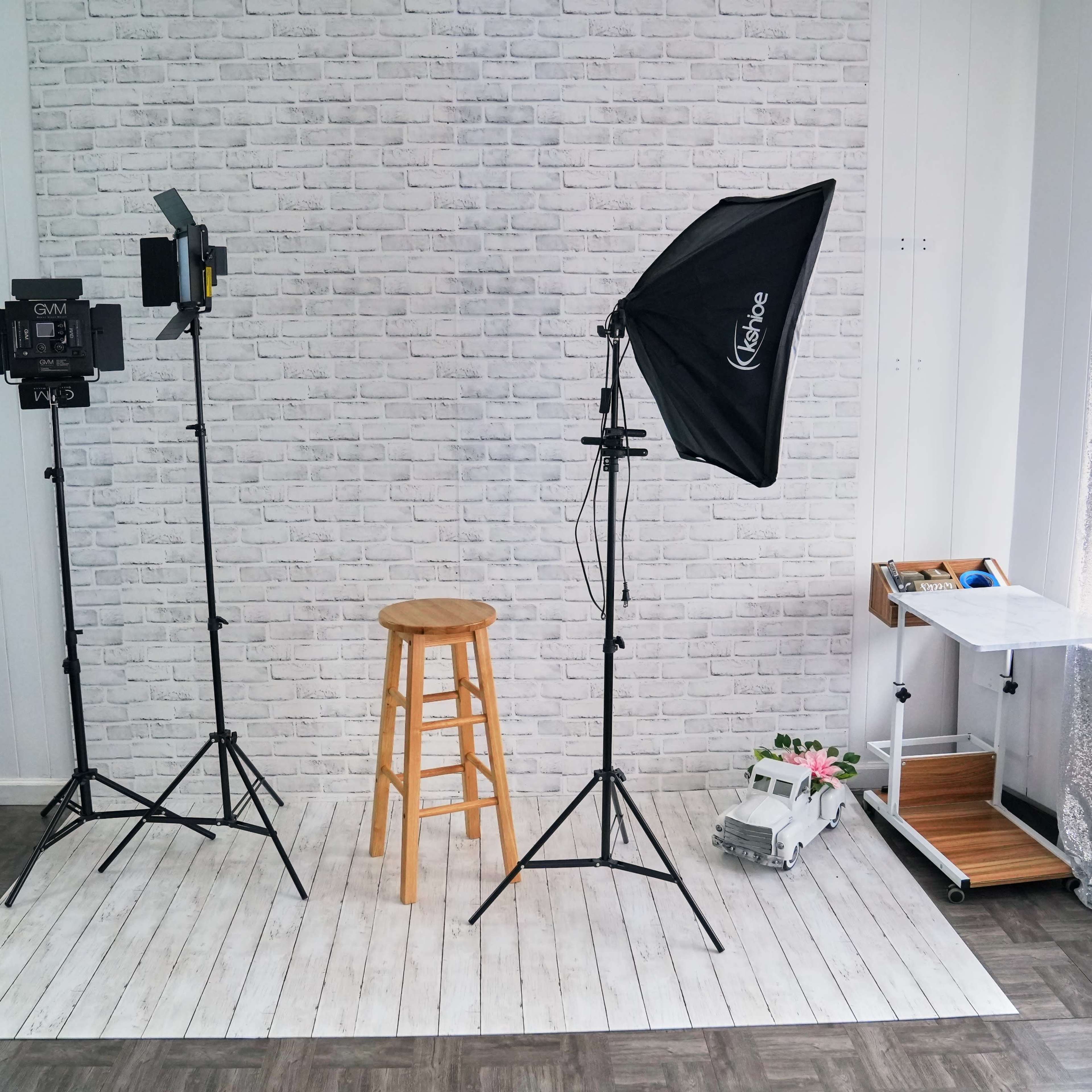A photography studio setup featuring a stool, lighting equipment, and a backdrop against a white brick wall.