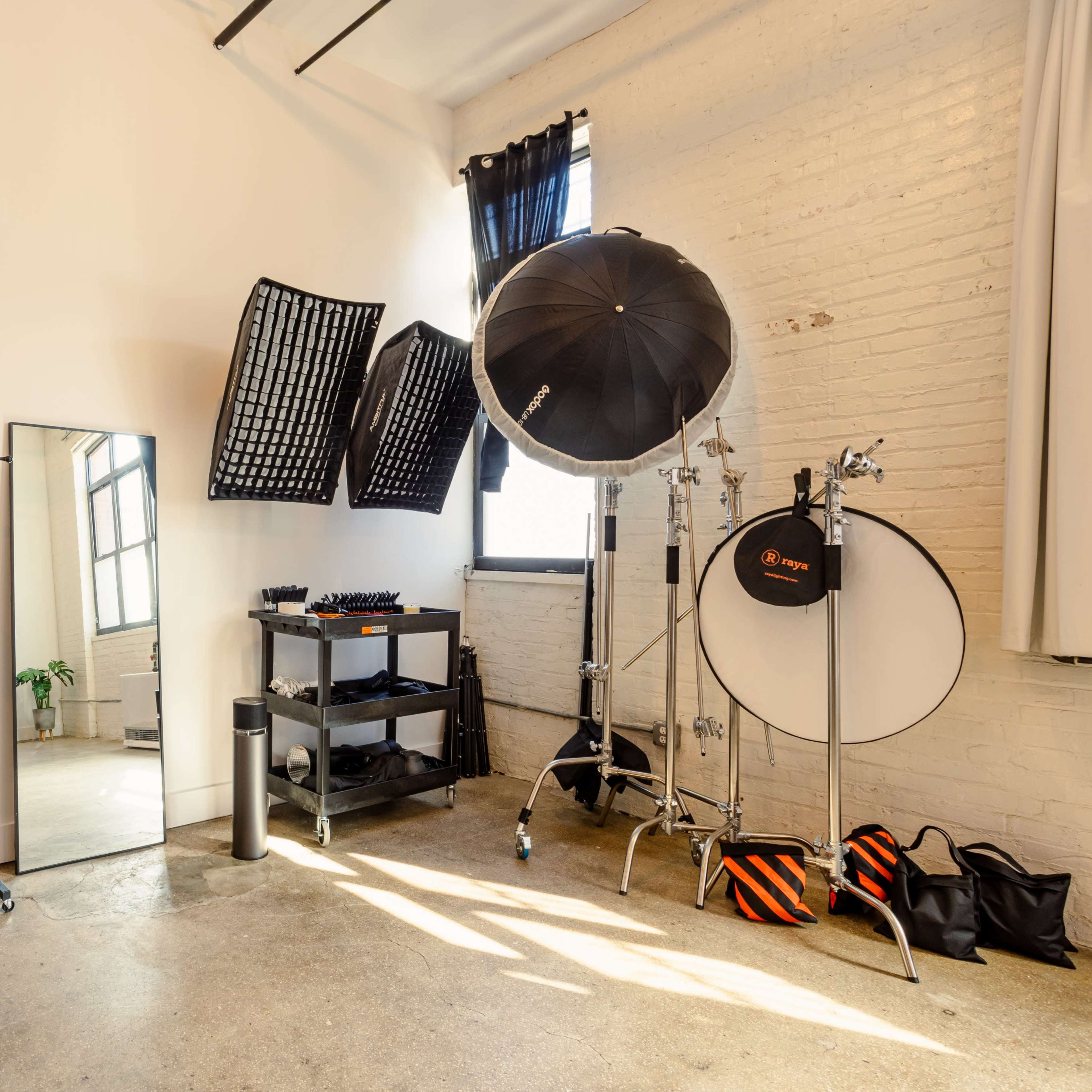 A photography studio features a large mirror, a clothing rack, various lighting equipment, and large windows letting in natural light.