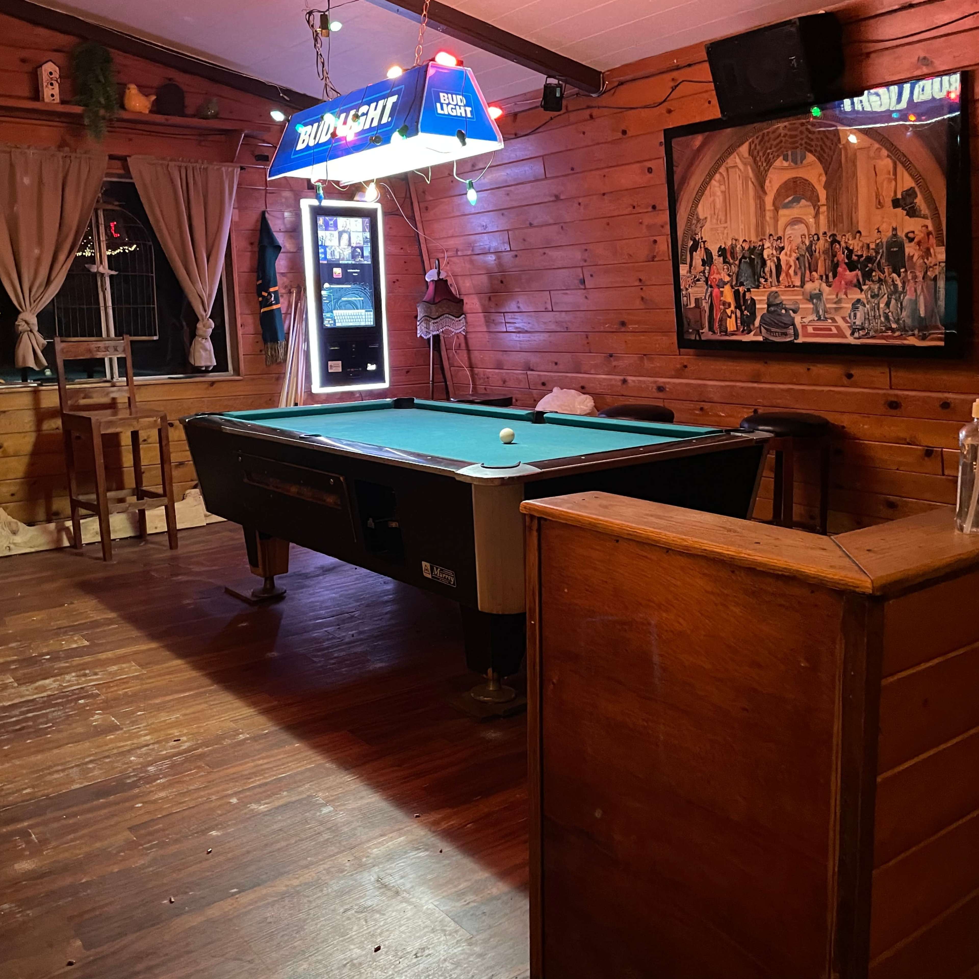 A wooden-paneled room with a pool table, a bar area, and a vintage-style illuminated sign.