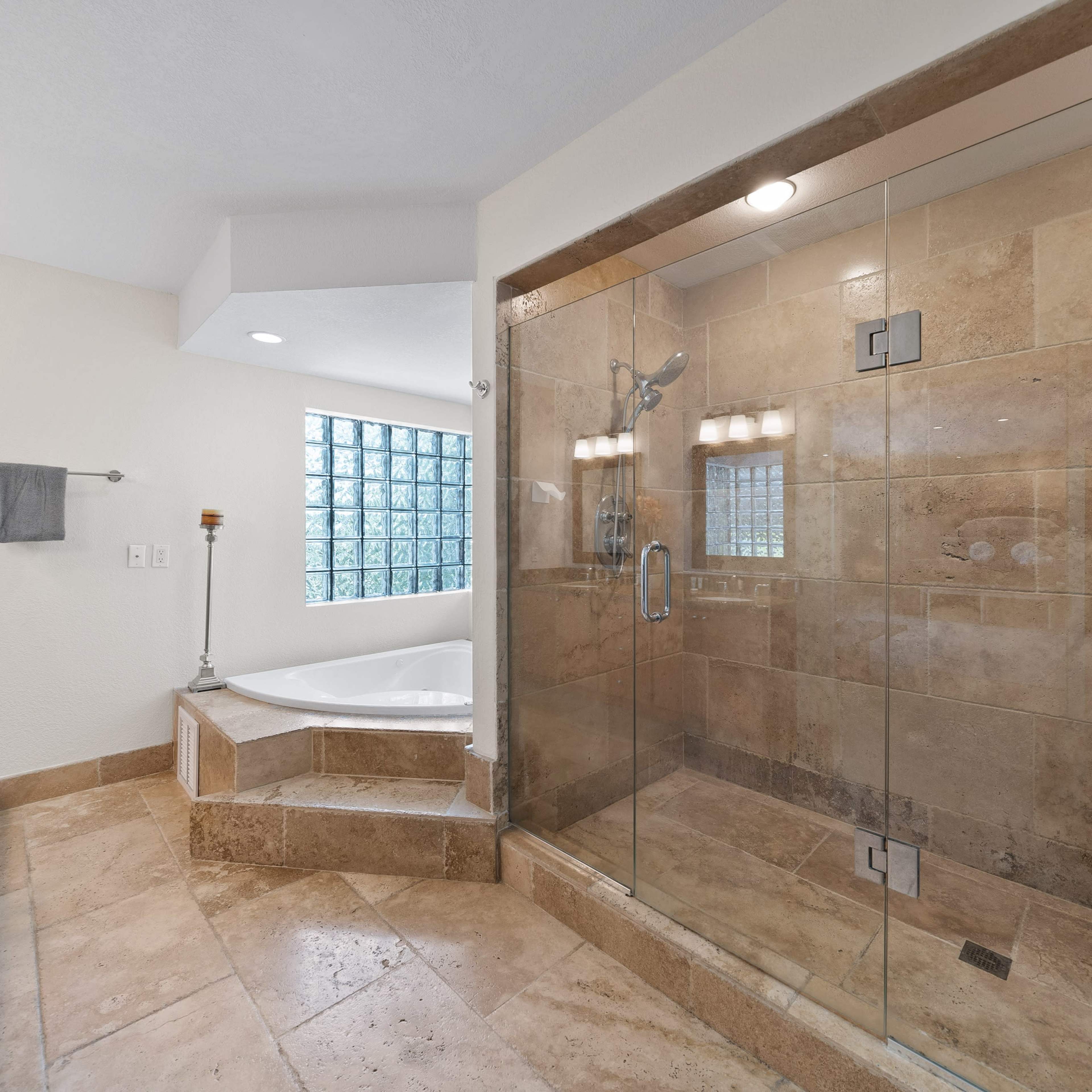 A spacious bathroom featuring a glass-enclosed shower, a large bathtub, and a tiled floor.