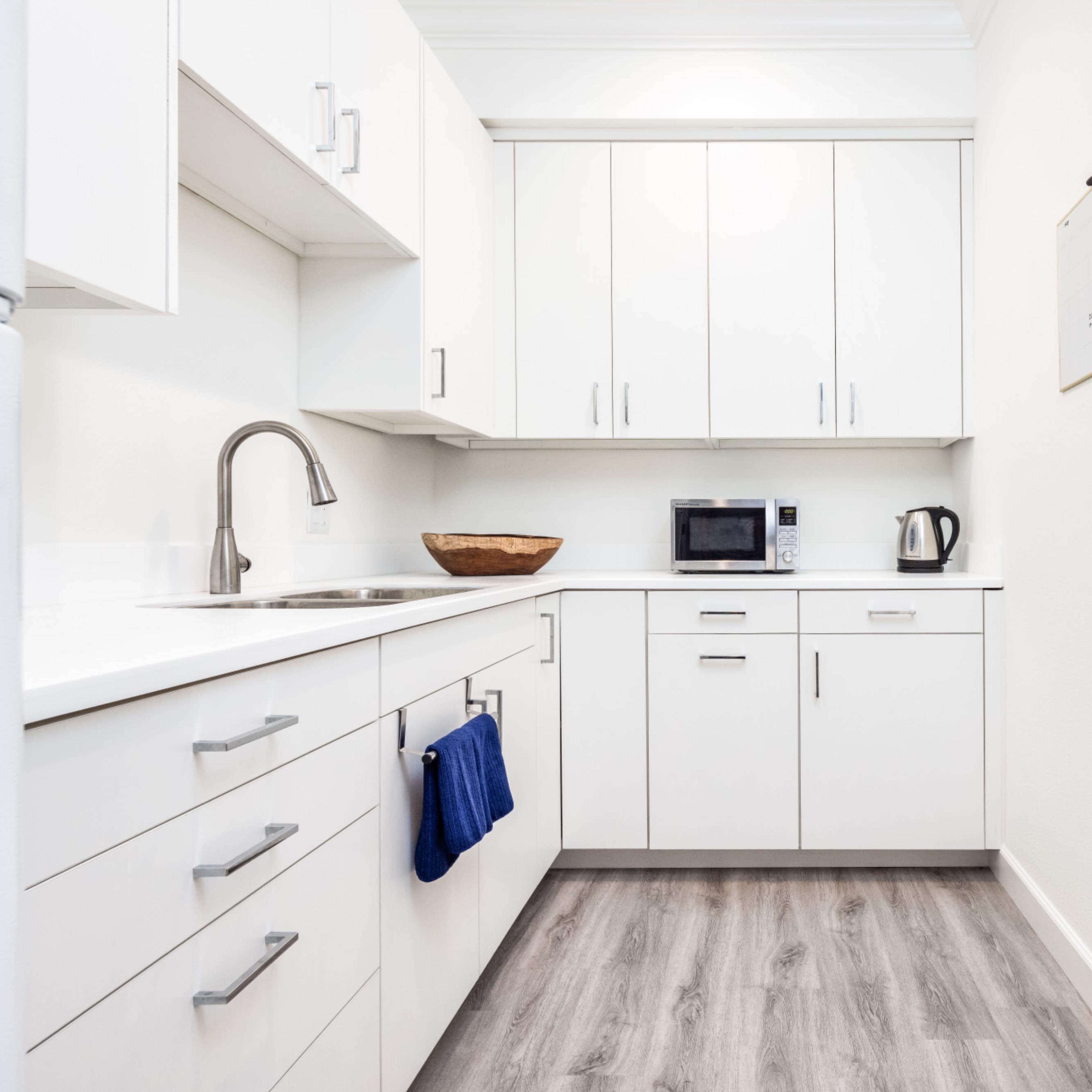 A modern kitchen with white cabinets, a sink, and appliances including a microwave and kettle.