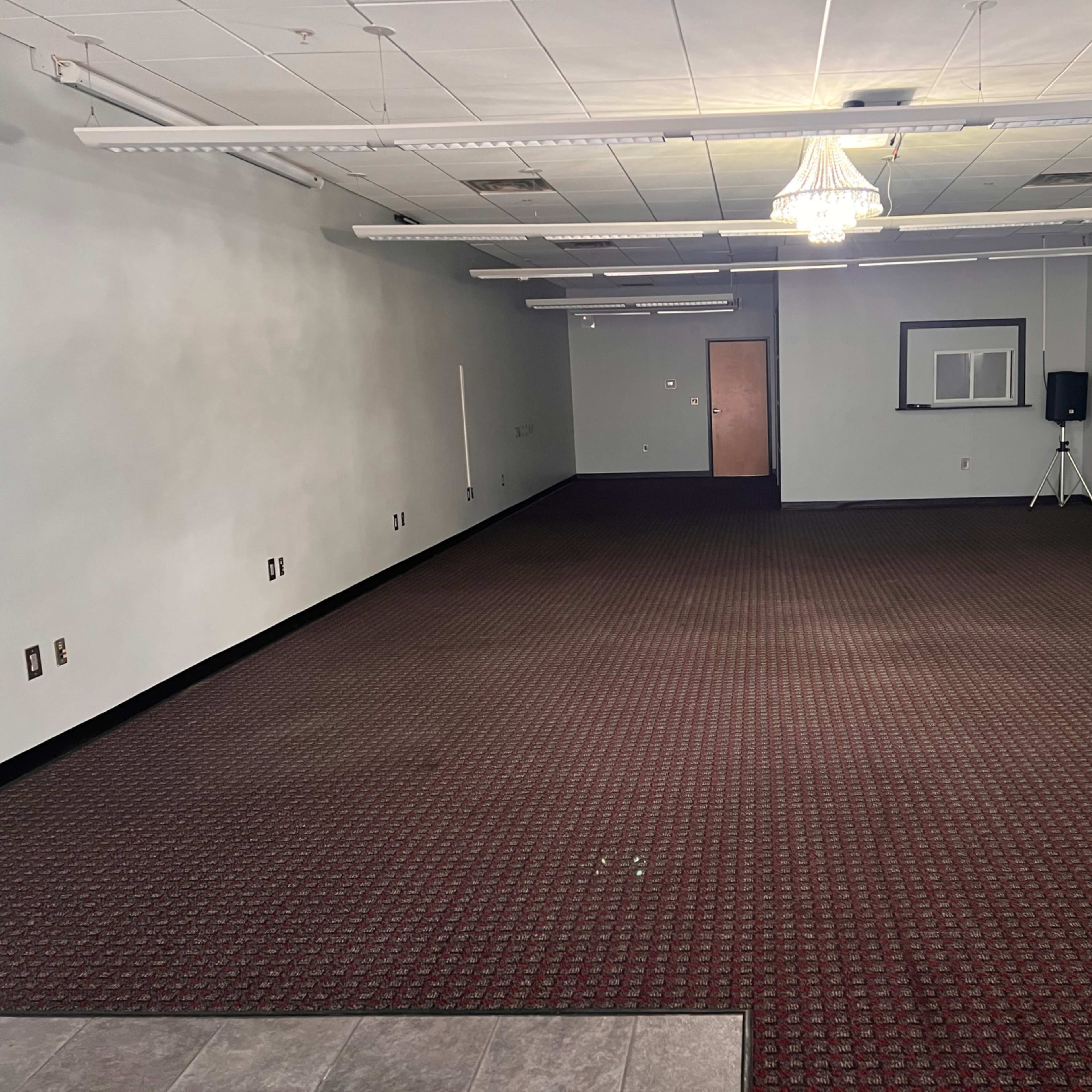 An empty room with a carpeted floor, walls painted in a light color, and a chandelier hanging from the ceiling.