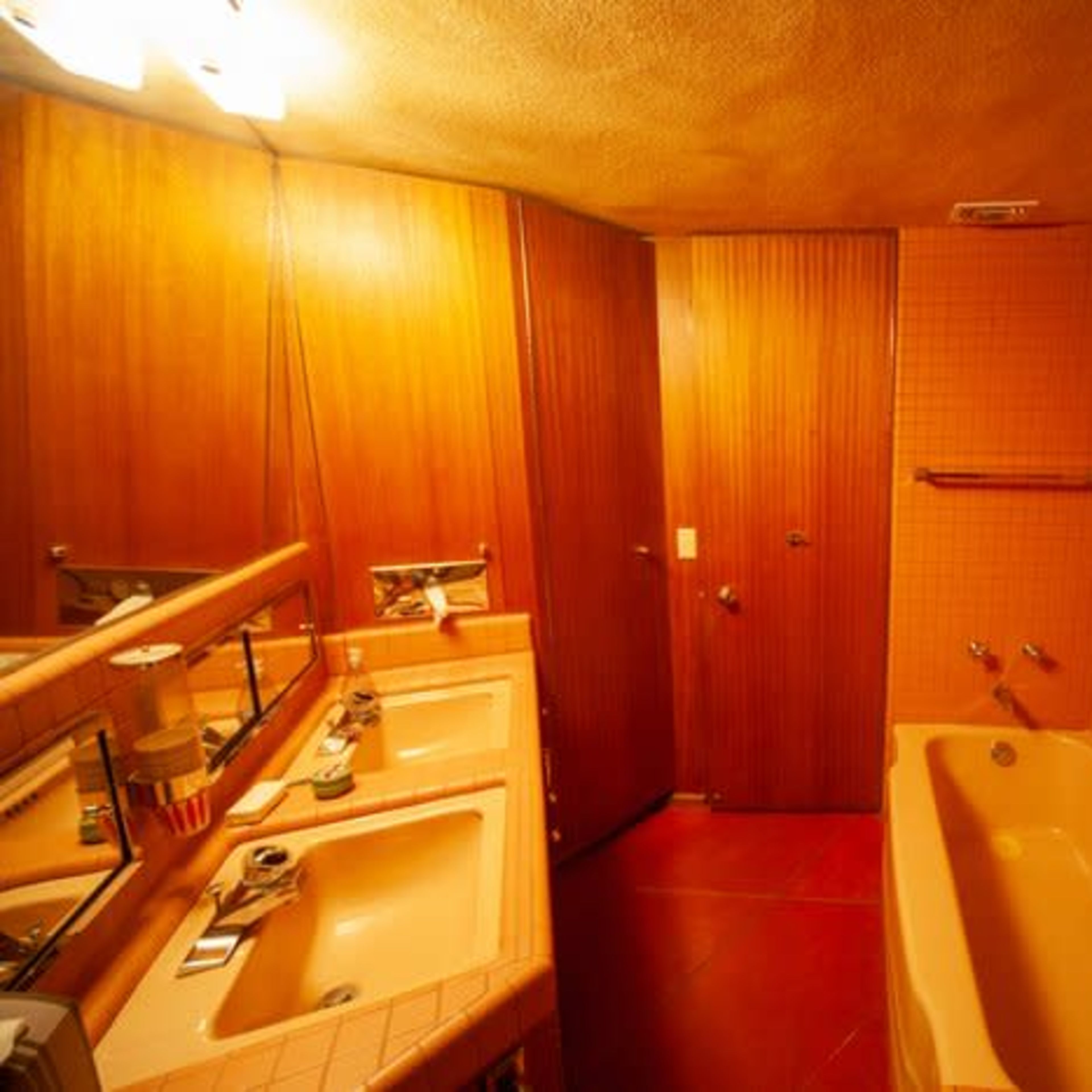 A bathroom with orange tiled walls, a pink bathtub, and dual sinks, all set against wood paneling.