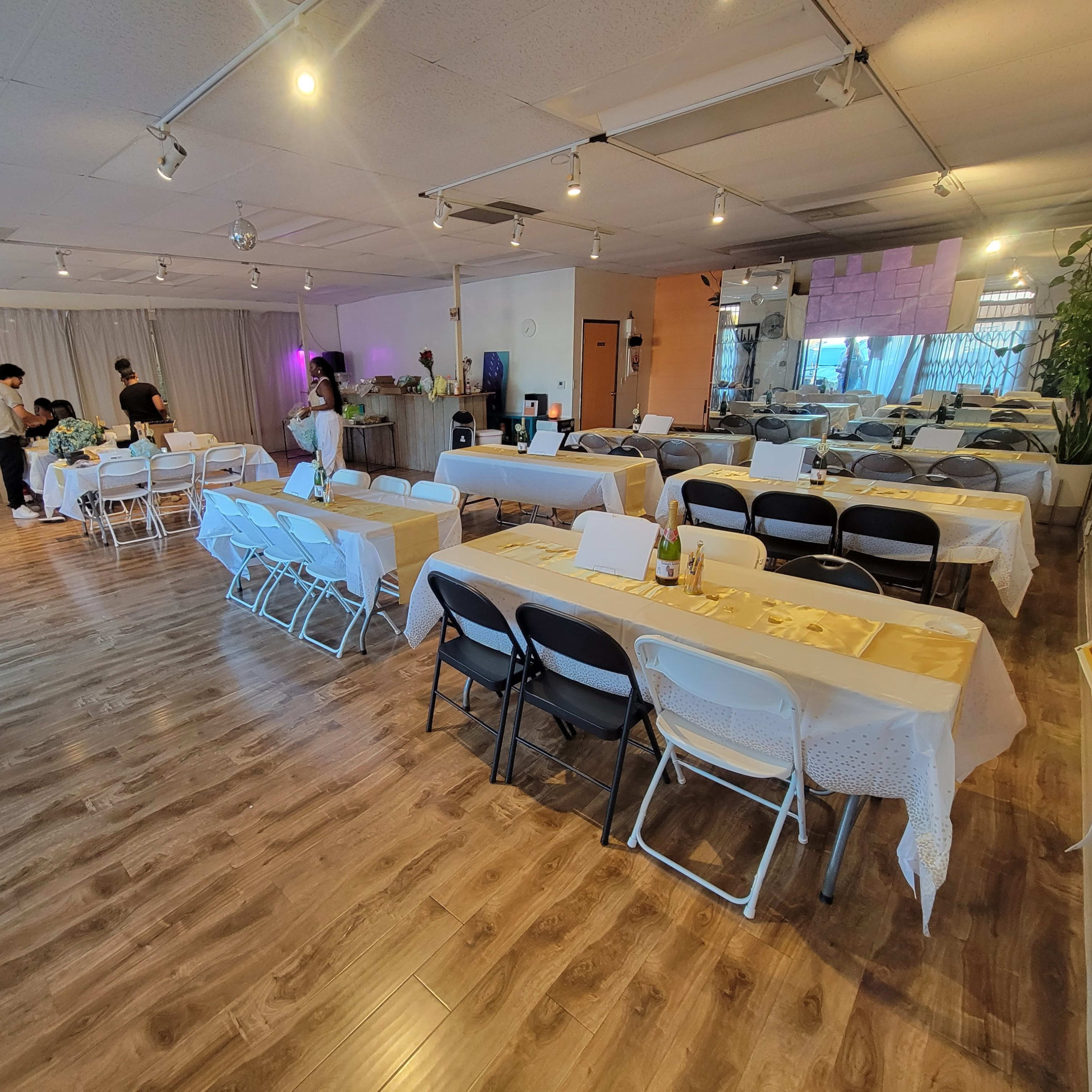 A spacious event room set up with tables and chairs, where people are preparing for an upcoming gathering.